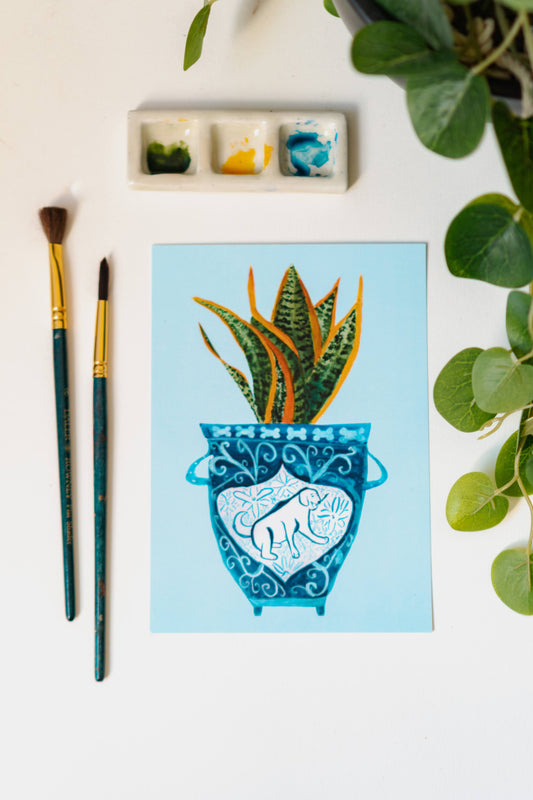 A print of a snake plant in a blue and white porcelain vase, decorated with a dog.
