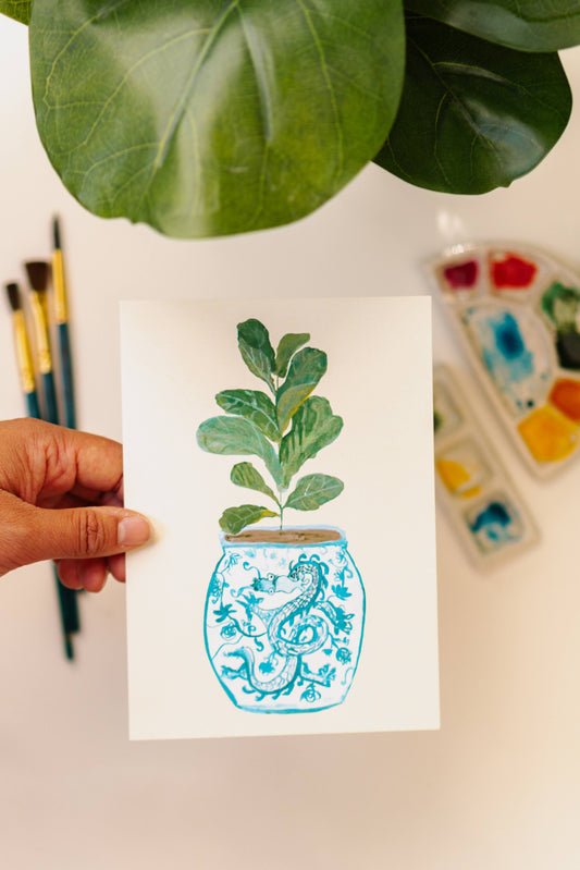 A print of a fiddle-leaf fig plant in a blue and white porcelain vase, decorated with a dragon.