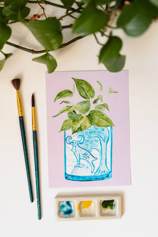 A print of a pothos plant in a blue and white porcelain vase, decorated with a goat.