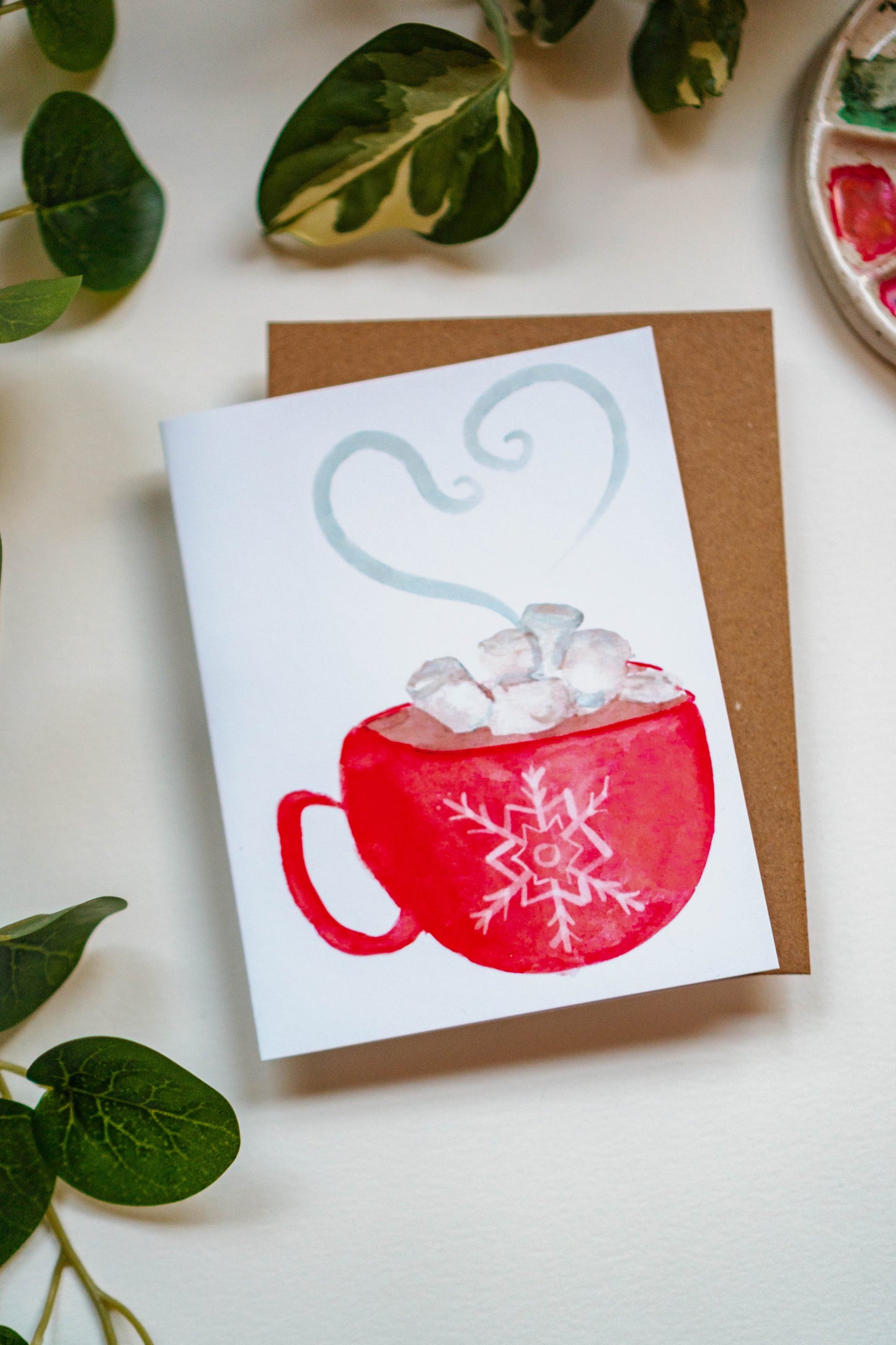 A greeting card with a steaming mug of hot chocolate. A red mug embellished with a snowflake holds hot cocoa and marshmallows.