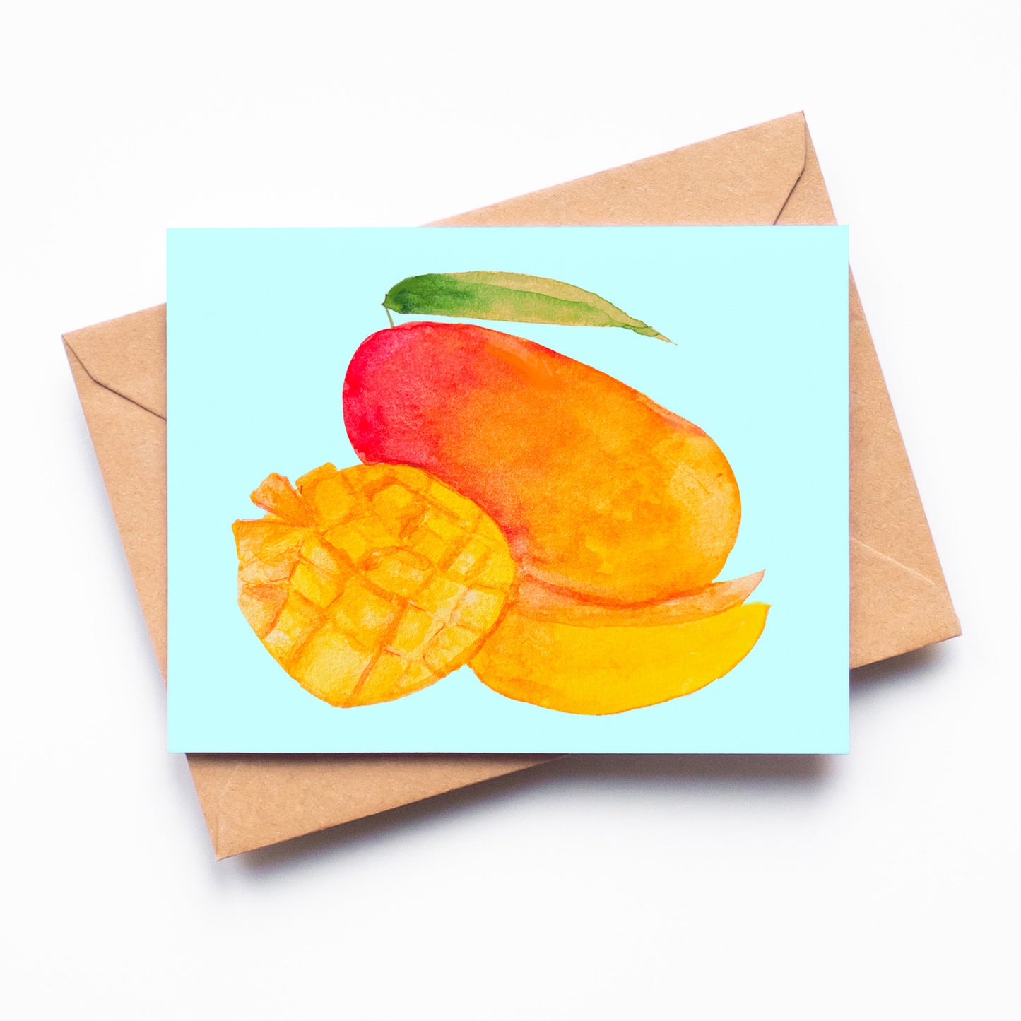 A light blue card with a red and orange mango on it. A cubed mango and a mango slice rests in front of a whole mango on the card.