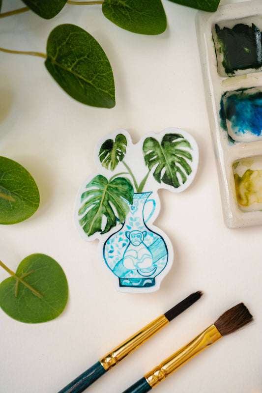 A sticker of a monstera plant in a blue and white porcelain vase, decorated with a monkey.
