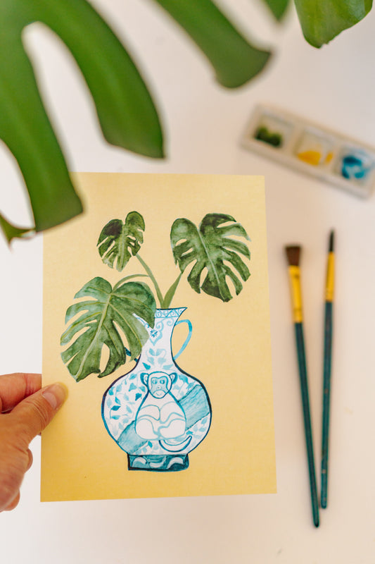 A print of a monstera plant in a blue and white porcelain vase, decorated with a monkey.