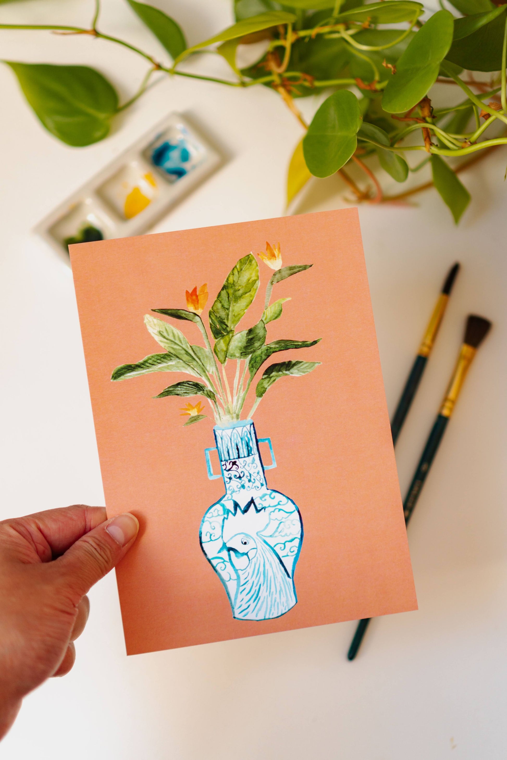 A print of a bird of paradise plant in a blue and white porcelain vase, decorated with a rooster.