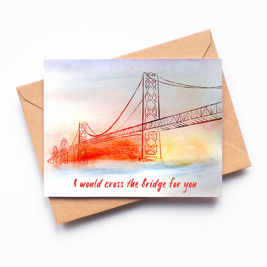 A card with a watercolor rendition of the San Francisco Bay Bridge on it, painted in oranges, yellows, and blues. The phrase "I would cross the bridge for you" is written on the bottom of the card.