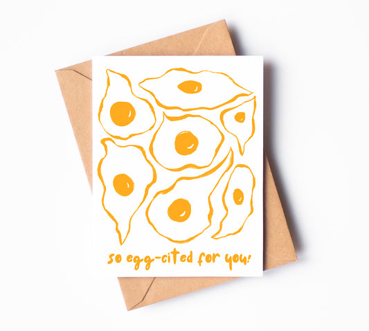 A greeting card with seven sunny side up eggs drawn in yellow ink and the phrase "so egg-cited for you!"