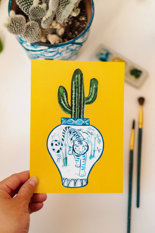 A print of a saguaro cactus in a blue and white porcelain vase, decorated with a tiger.