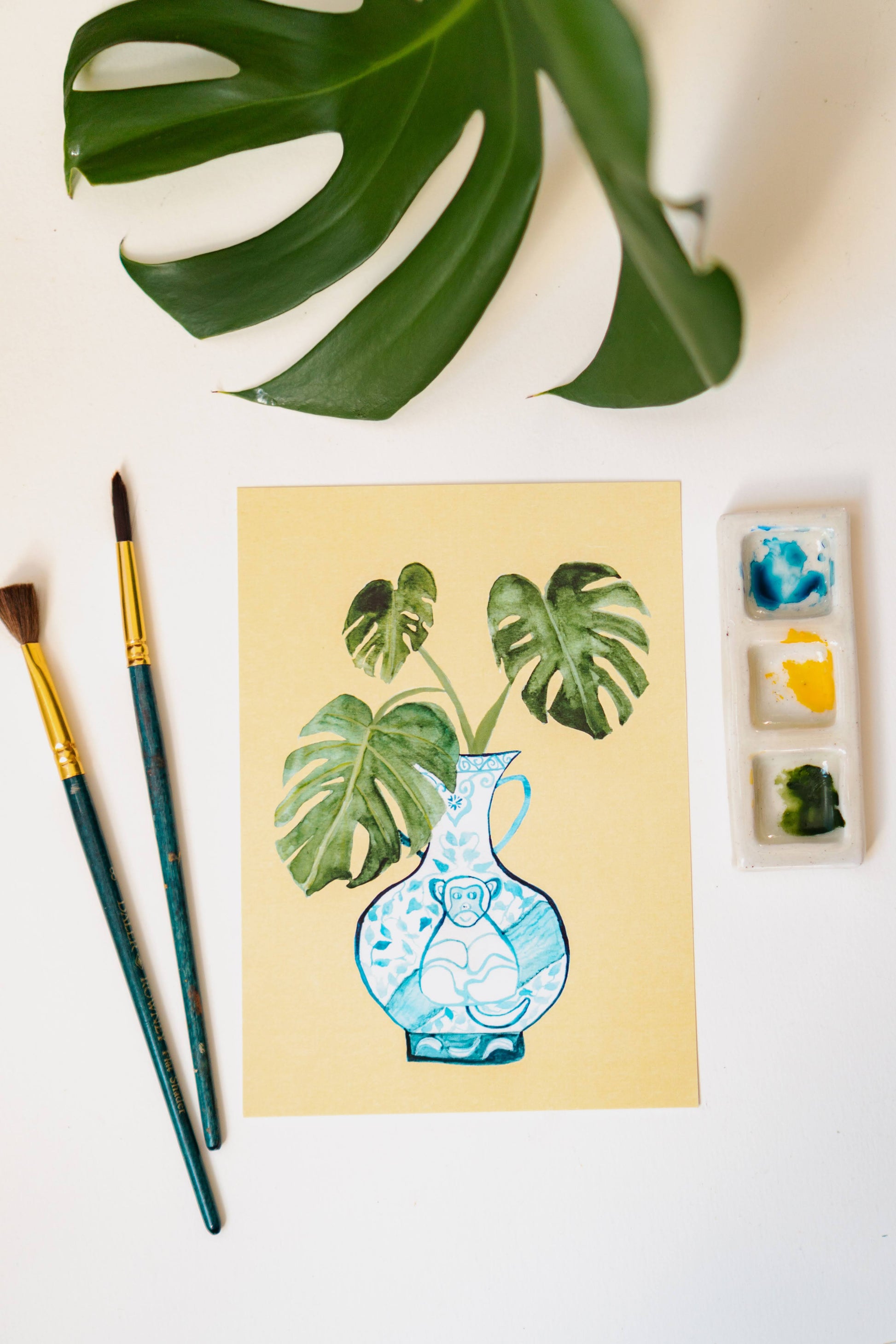 A print of a monstera plant in a blue and white porcelain vase, decorated with a monkey.