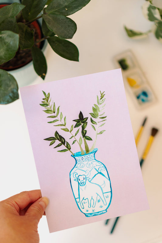 A print of a ZZ plant in a blue and white porcelain vase, decorated with an ox.