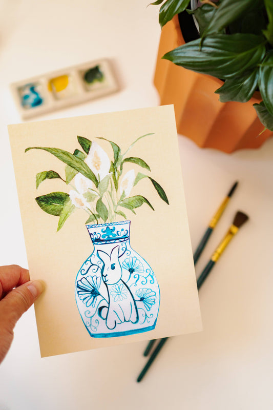 A print of a peace lily plant in a blue and white porcelain vase, decorated with a rabbit.