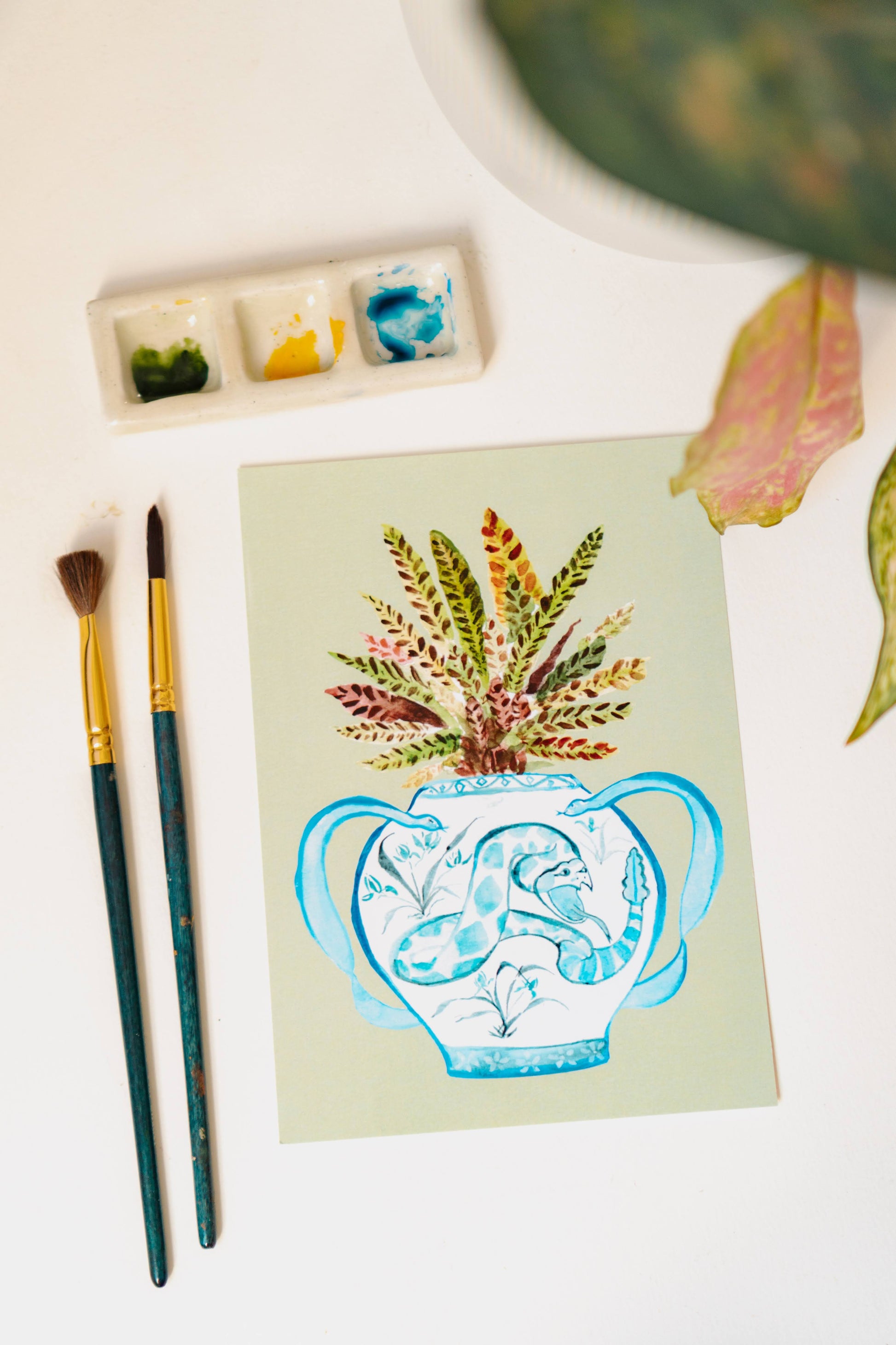 A print of a rattlesnake plant in a blue and white porcelain vase, decorated with a snake.