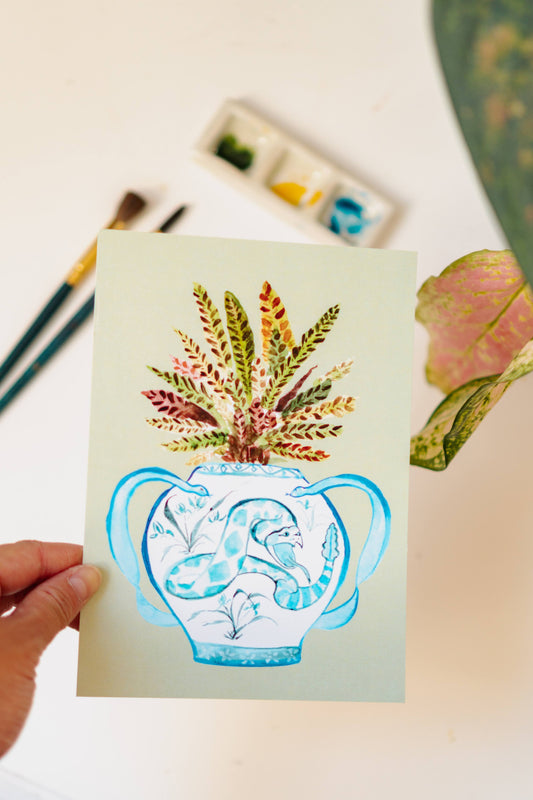 A print of a rattlesnake plant in a blue and white porcelain vase, decorated with a snake.