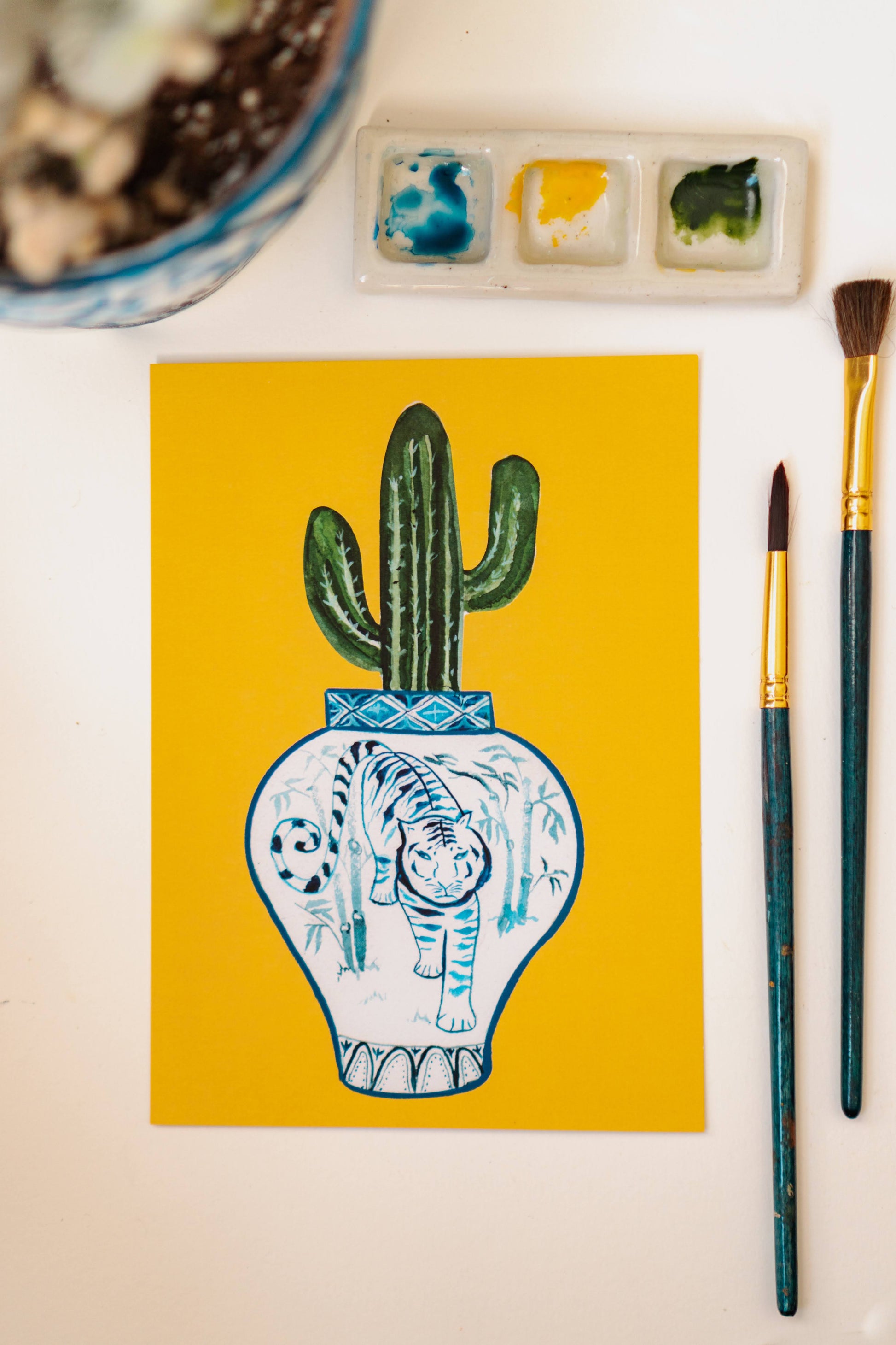 A print of a saguaro cactus in a blue and white porcelain vase, decorated with a tiger.