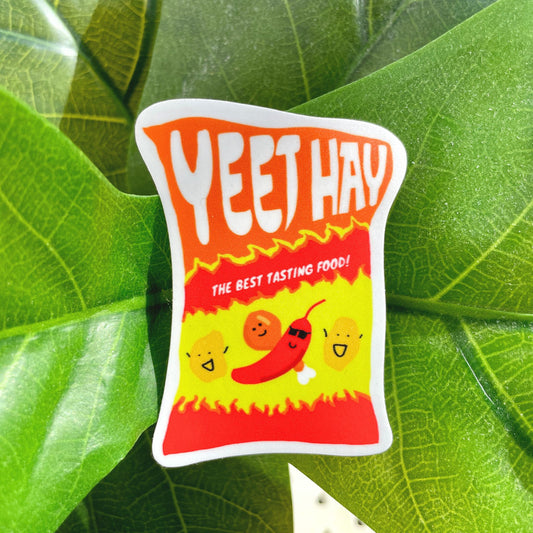A sticker of a spicy bag of chips, drawn with red-yellow flames and smiling spicy foods, including a chili with sunglasses. "Yeet Hay" is written across the top of the bag, and below is written, "The best tasting food!"