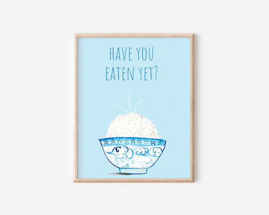 A light blue and white asian art print with the phrase, "Have you eaten yet?" written across the top. A steaming bowl of rice in a white and blue decorated bowl rests at the bottom of the print.