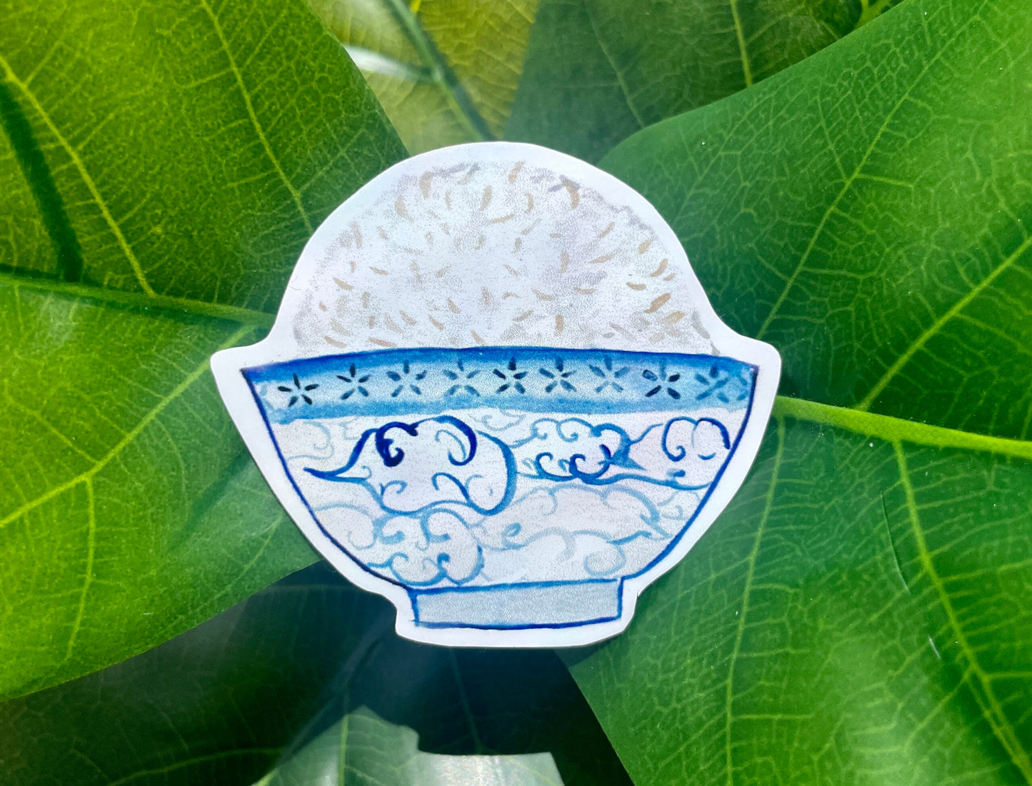 A white sticker of a blue and white watercolor bowl of rice. The bowl looks like porcelain and is decorated with blue line art clouds.