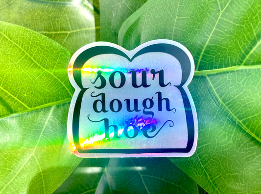 A holographic sticker featuring line art of a slice of bread and the words "sourdough hoe" written in the center.