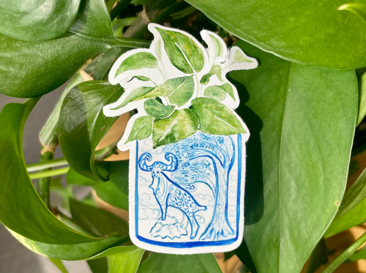 A sticker of a pothos plant in a blue and white porcelain vase, decorated with a goat.