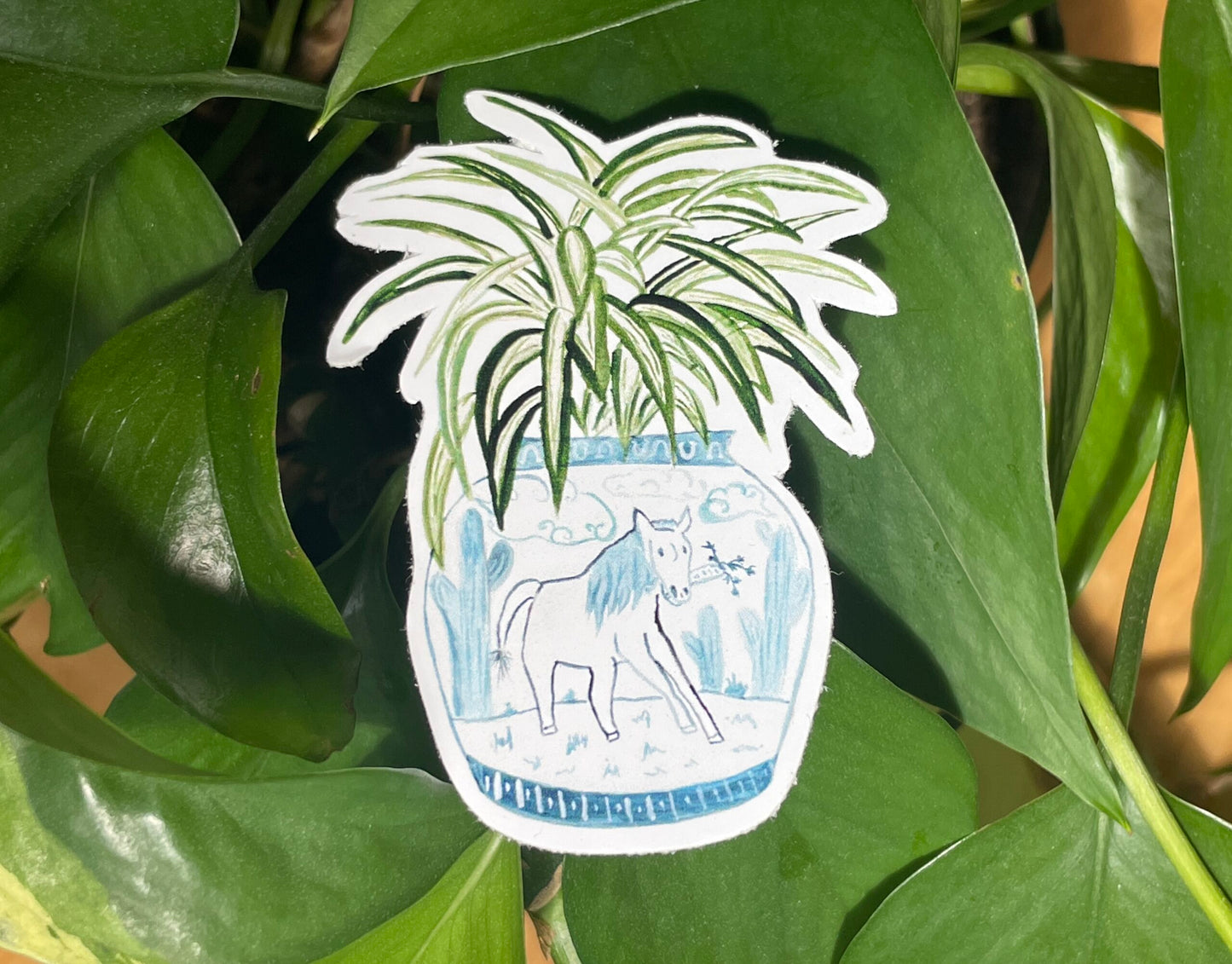 A sticker of a spider plant in a blue and white porcelain vase, decorated with a horse.