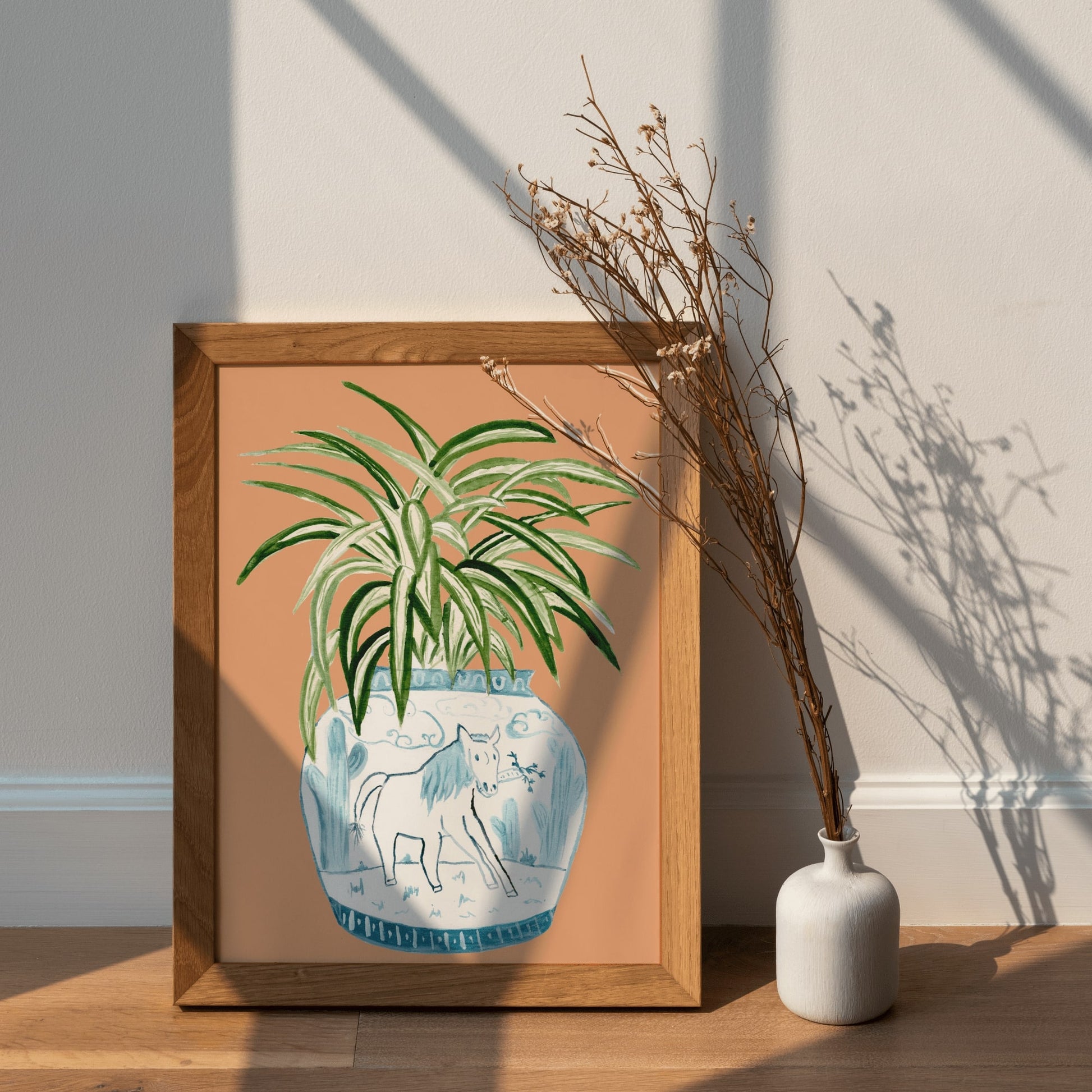 A print of a spider plant in a blue and white porcelain vase, decorated with a horse.
