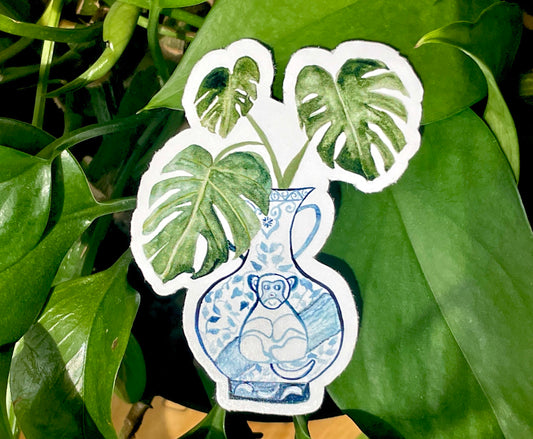 A sticker of a monstera plant in a blue and white porcelain vase, decorated with a monkey.