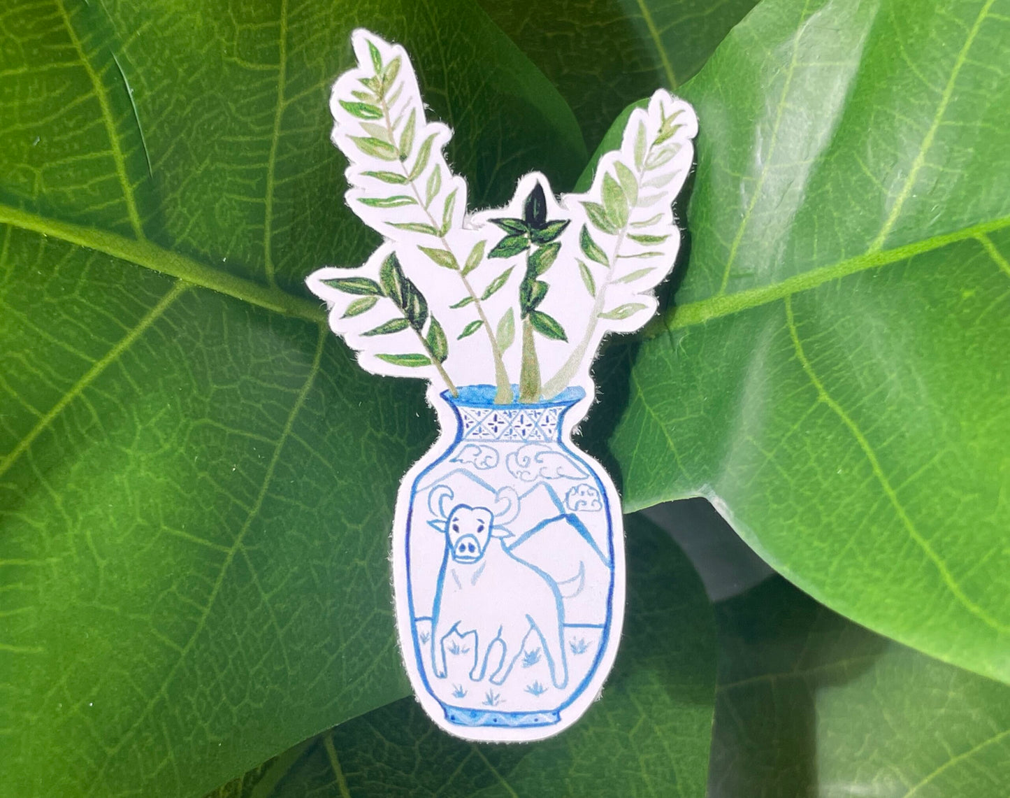 A sticker of a ZZ plant in a blue and white porcelain vase, decorated with an ox.