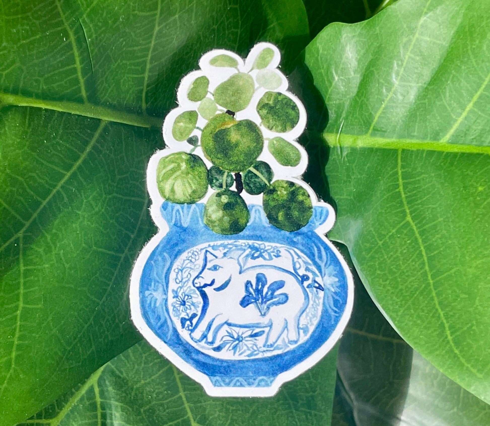 A sticker of a pilea plant in a blue and white porcelain vase, decorated with a pig.