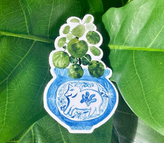 A sticker of a pilea plant in a blue and white porcelain vase, decorated with a pig.