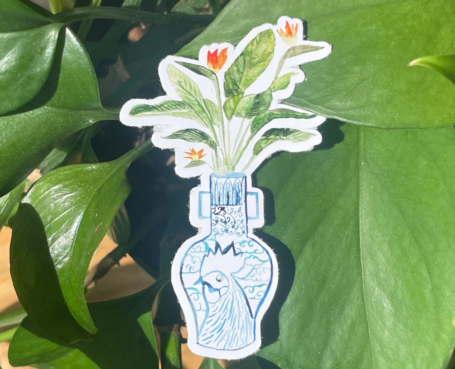 A sticker of a bird of paradise plant in a blue and white porcelain vase, decorated with a rooster.