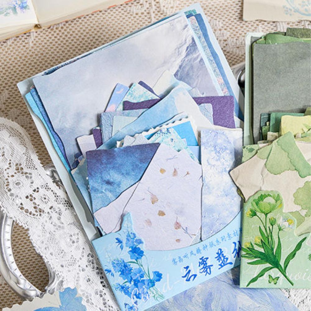Blue-toned scrapbook paper collection featuring floral, cloud, and marble designs with torn-edge and die-cut accents