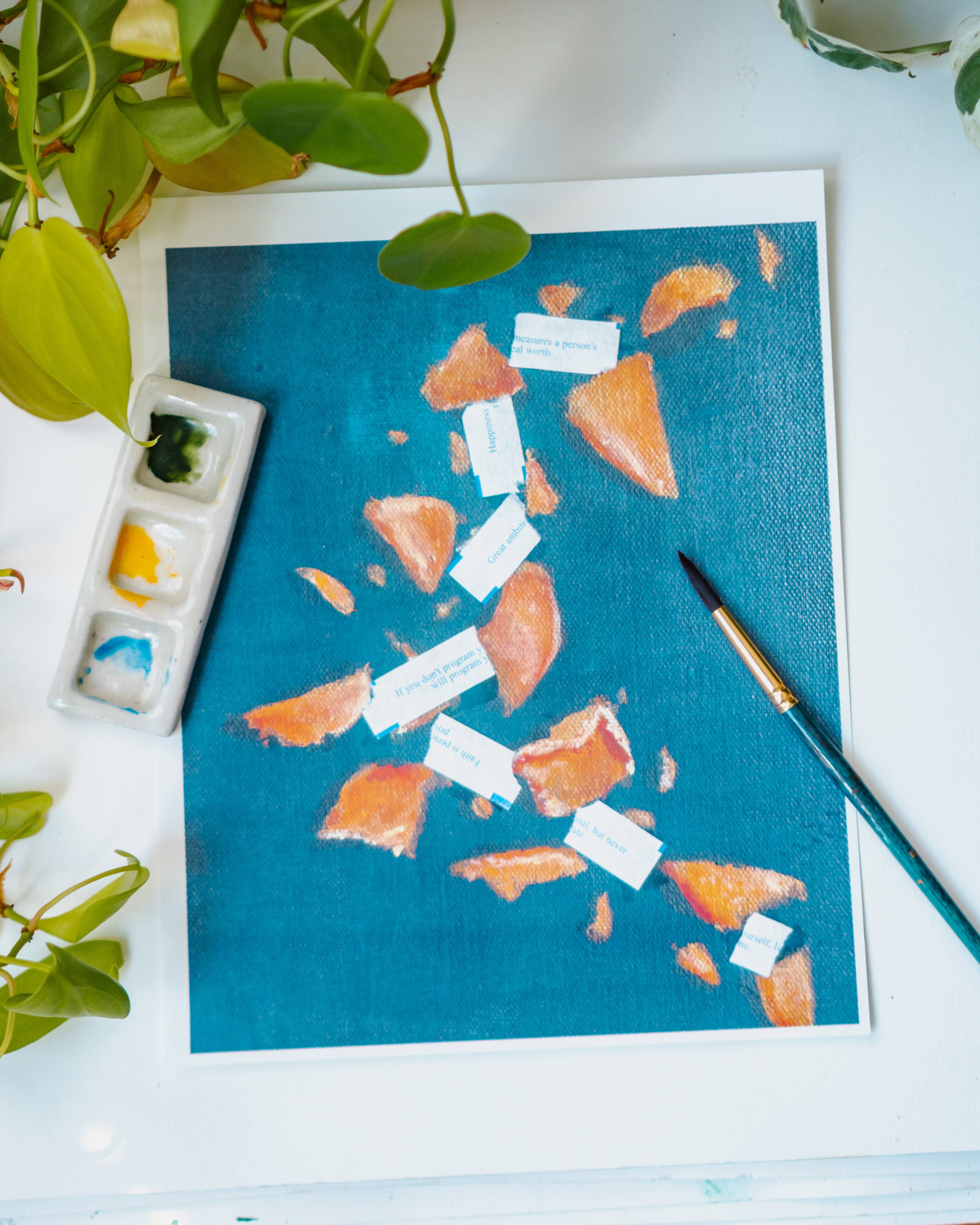 A watercolor print of broken fortune cookies and scattered fortunes on a blue background.