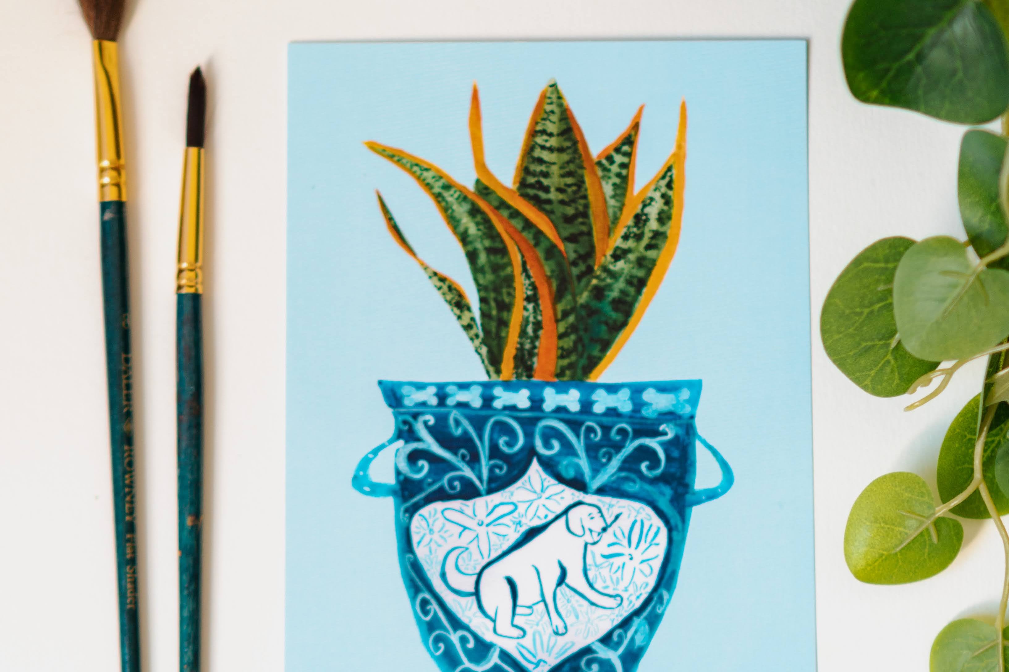 A print of a snake plant in a blue and white porcelain vase, decorated with a dog.