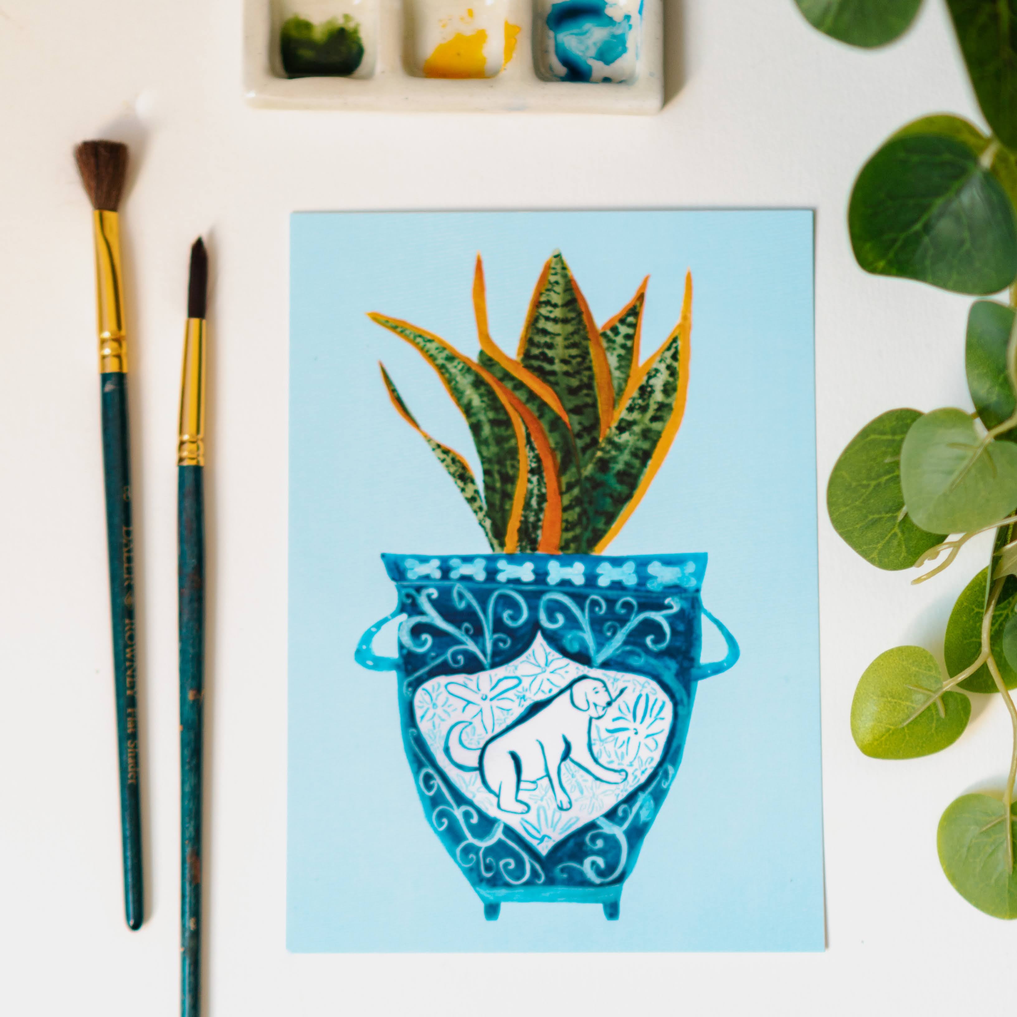 A print of a snake plant in a blue and white porcelain vase, decorated with a dog.