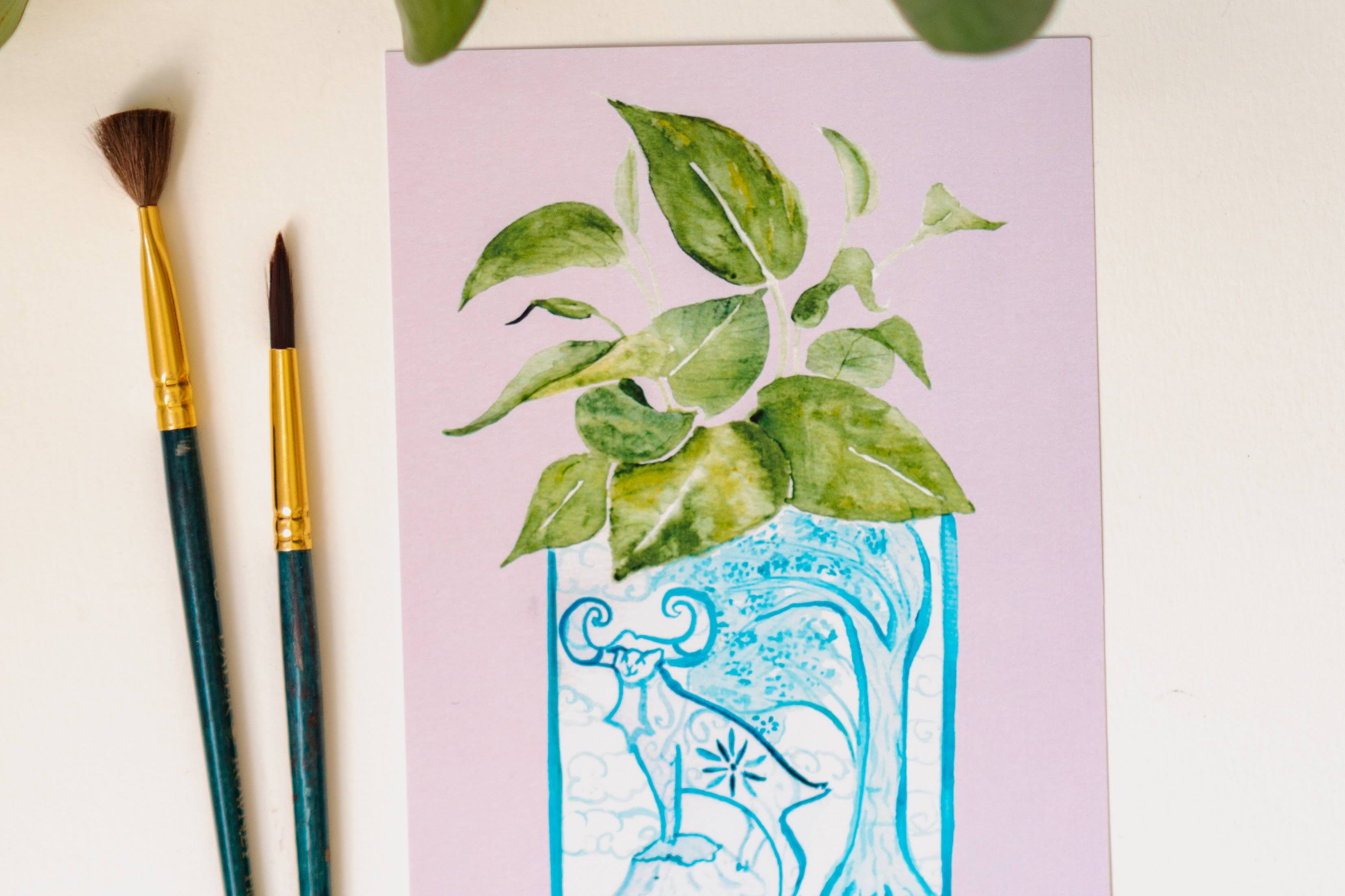 A print of a pothos plant in a blue and white porcelain vase, decorated with a goat.