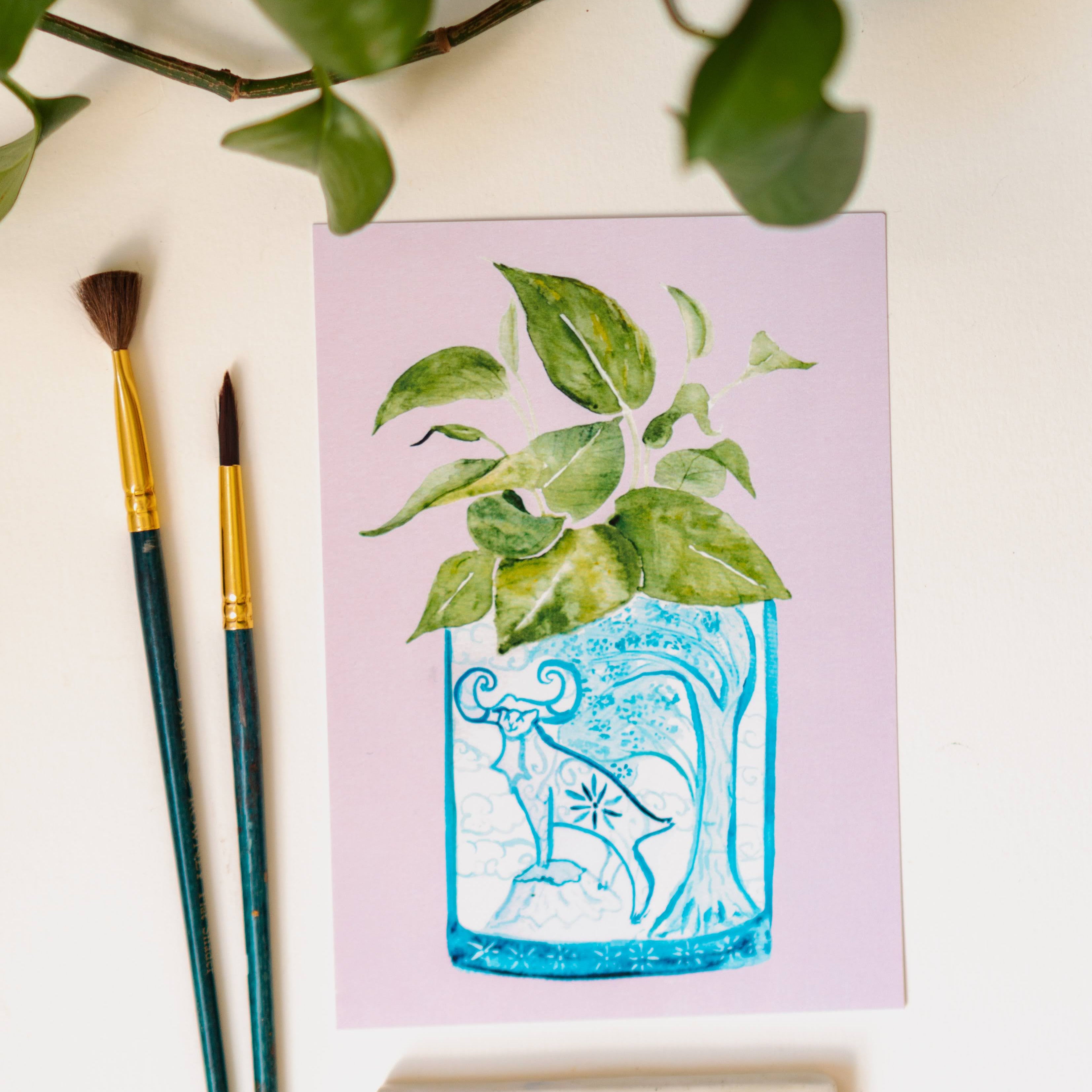 A print of a pothos plant in a blue and white porcelain vase, decorated with a goat.