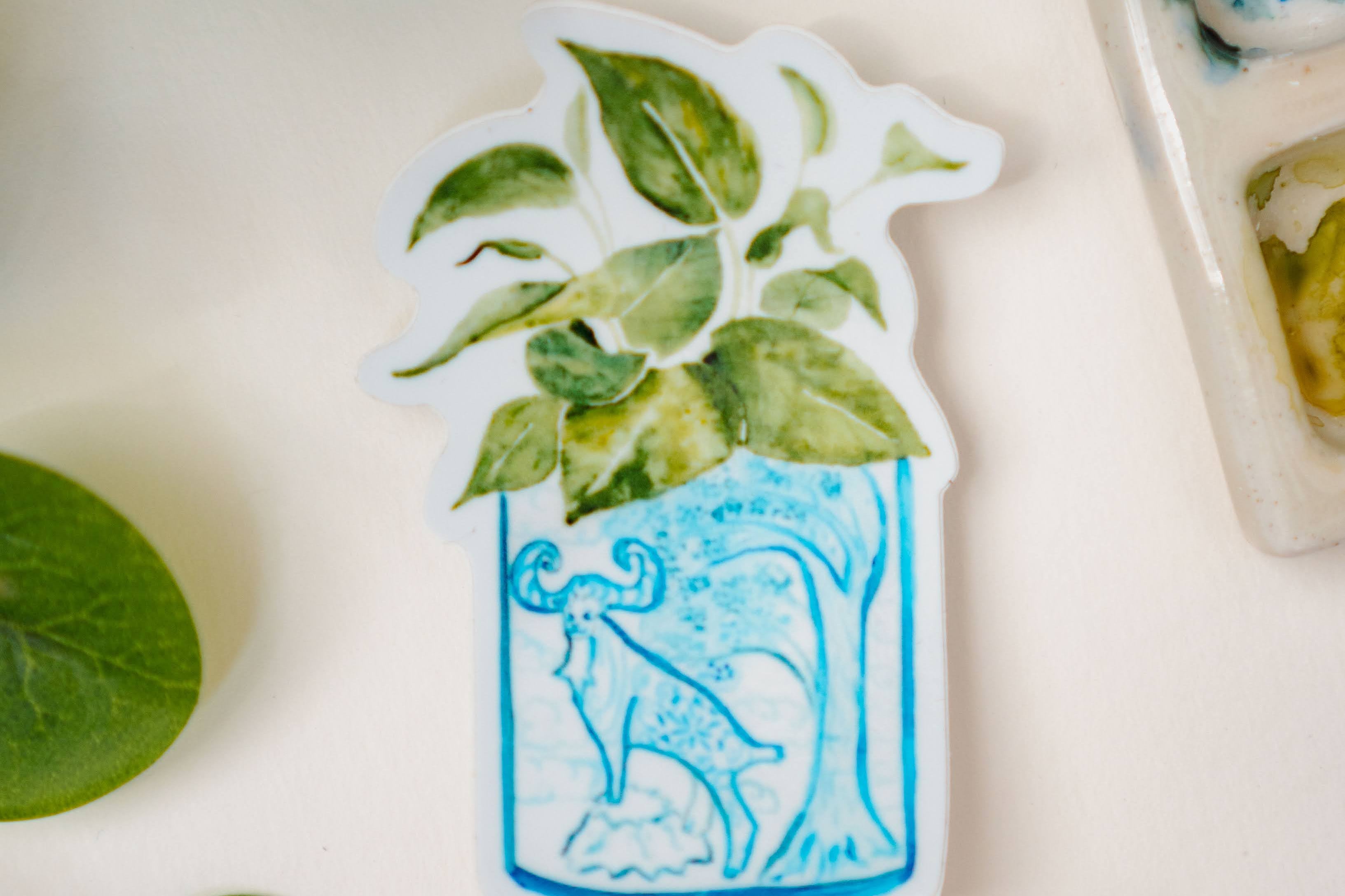 A sticker of a pothos plant in a blue and white porcelain vase, decorated with a goat.