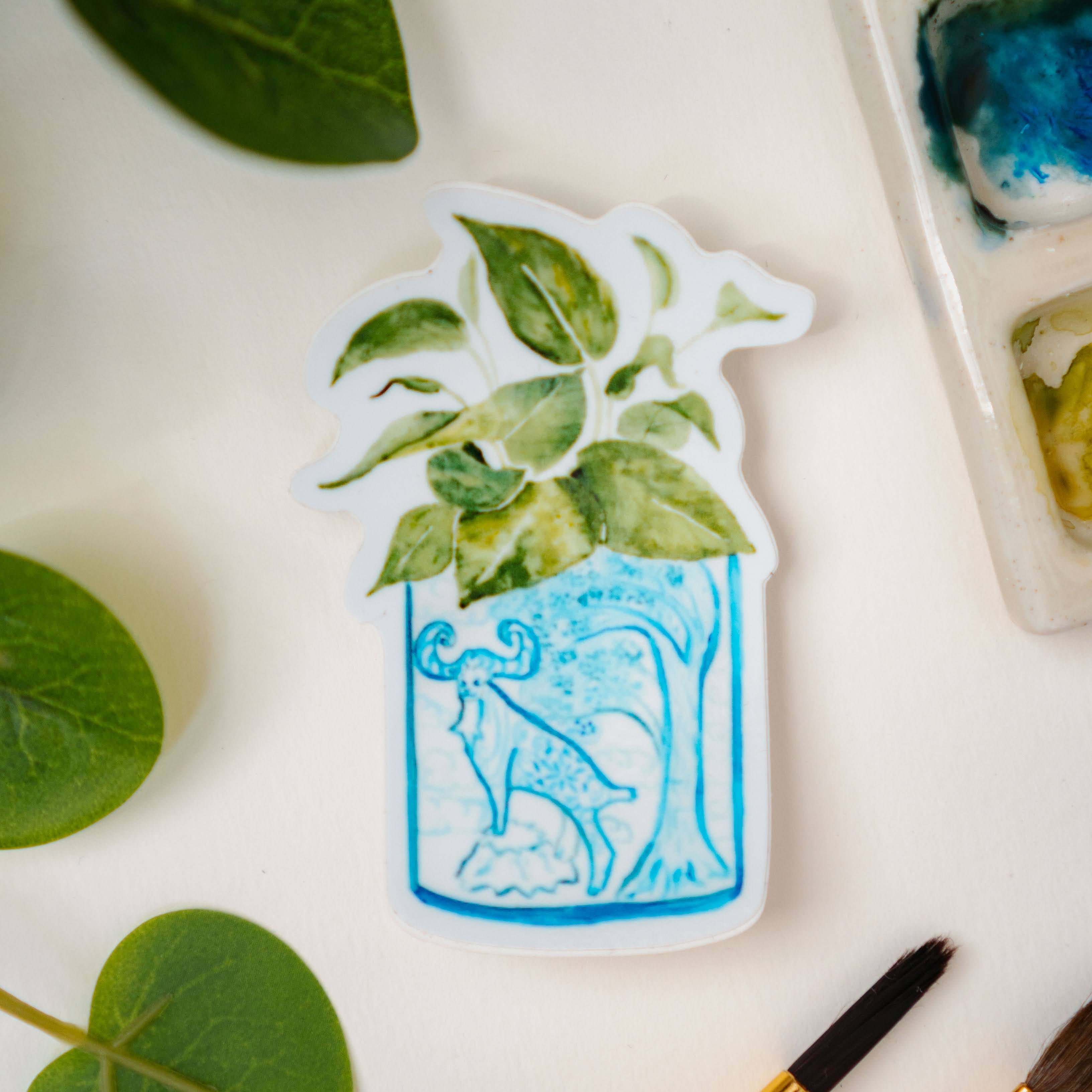 A sticker of a pothos plant in a blue and white porcelain vase, decorated with a goat.