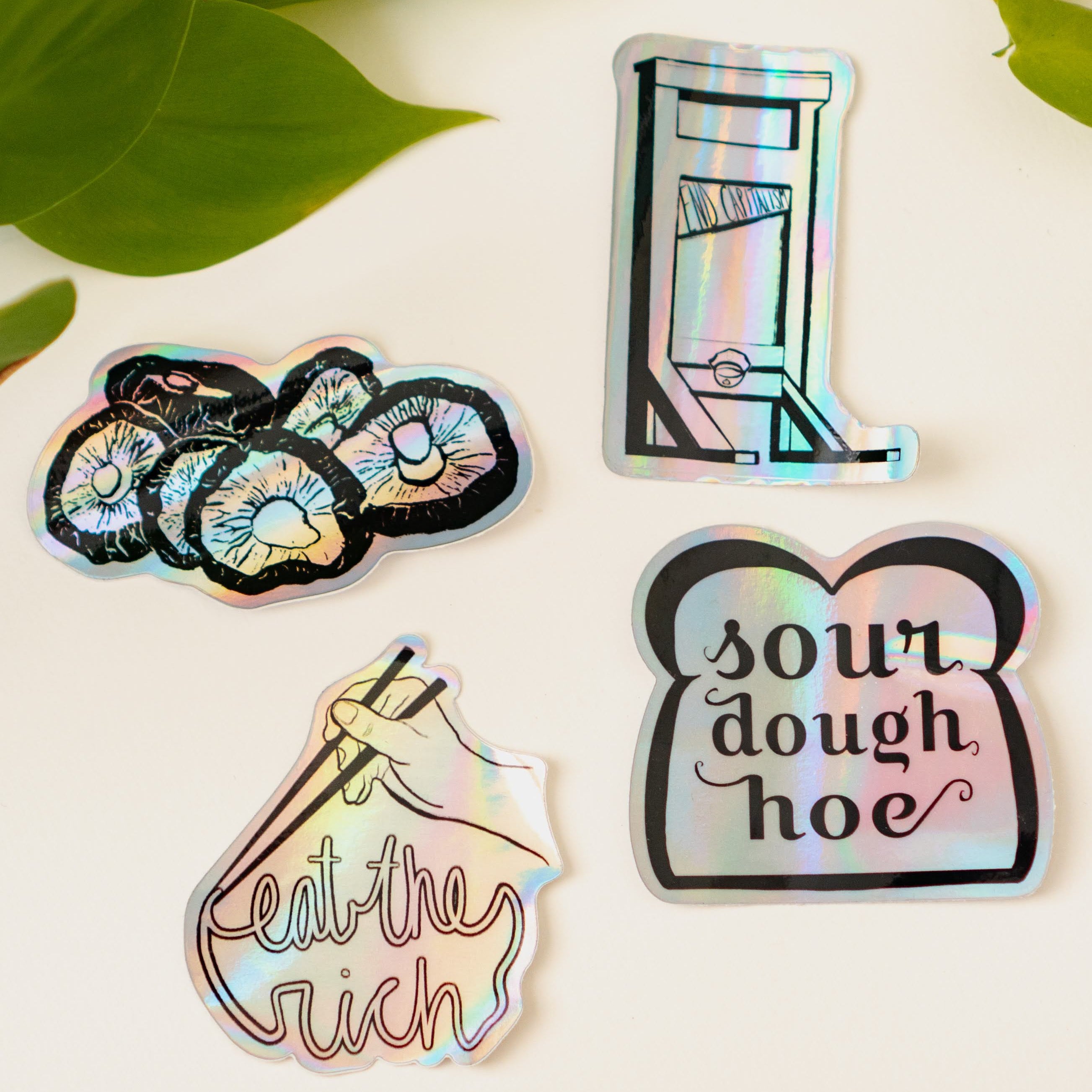 Menmin Made's four holographic stickers, including the Eat The Rich Sticker.