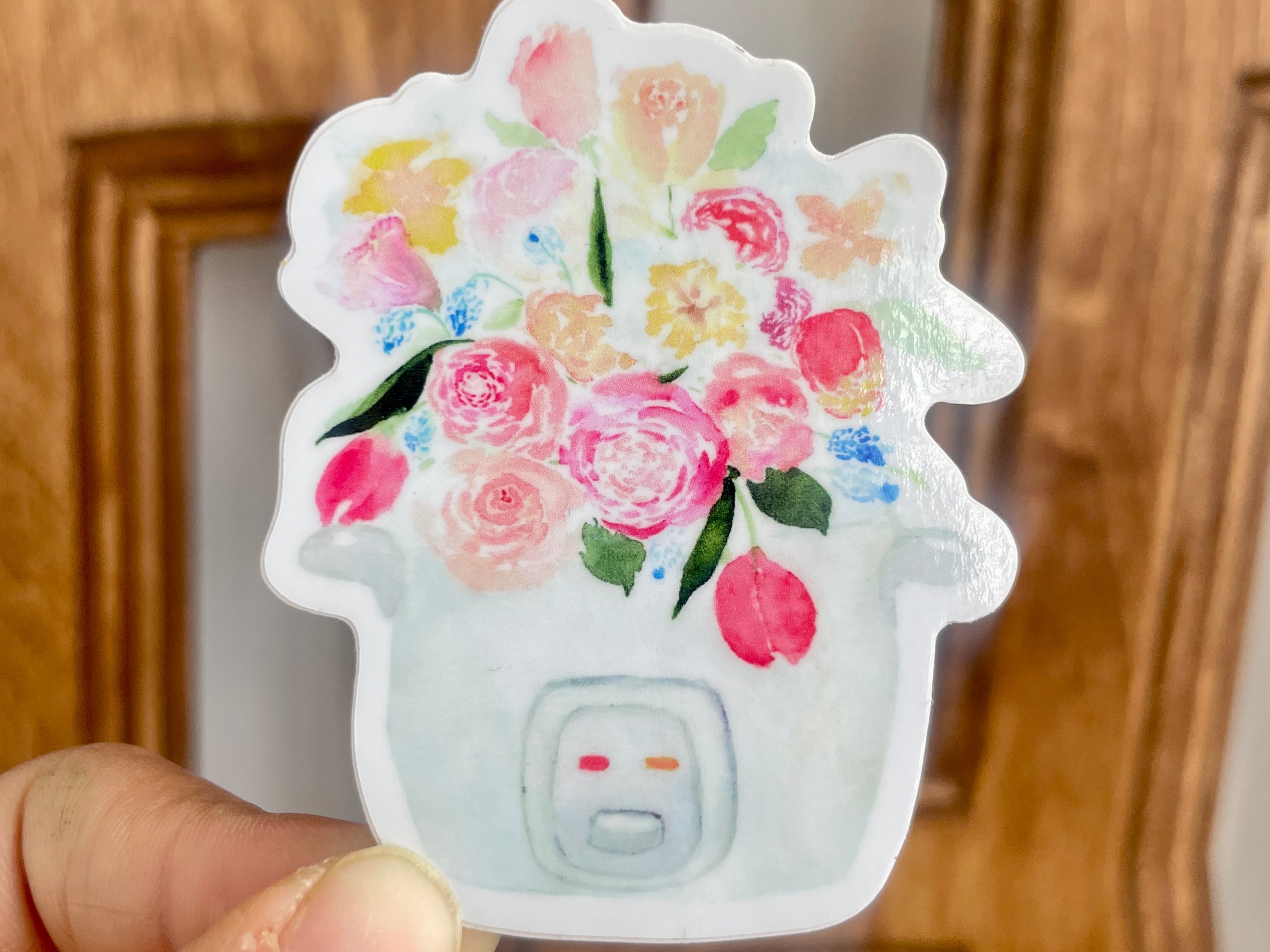 A pink, blue, and white sticker of a bouquet of tulips, roses, and other flowers sprouting out of a rice cooker.