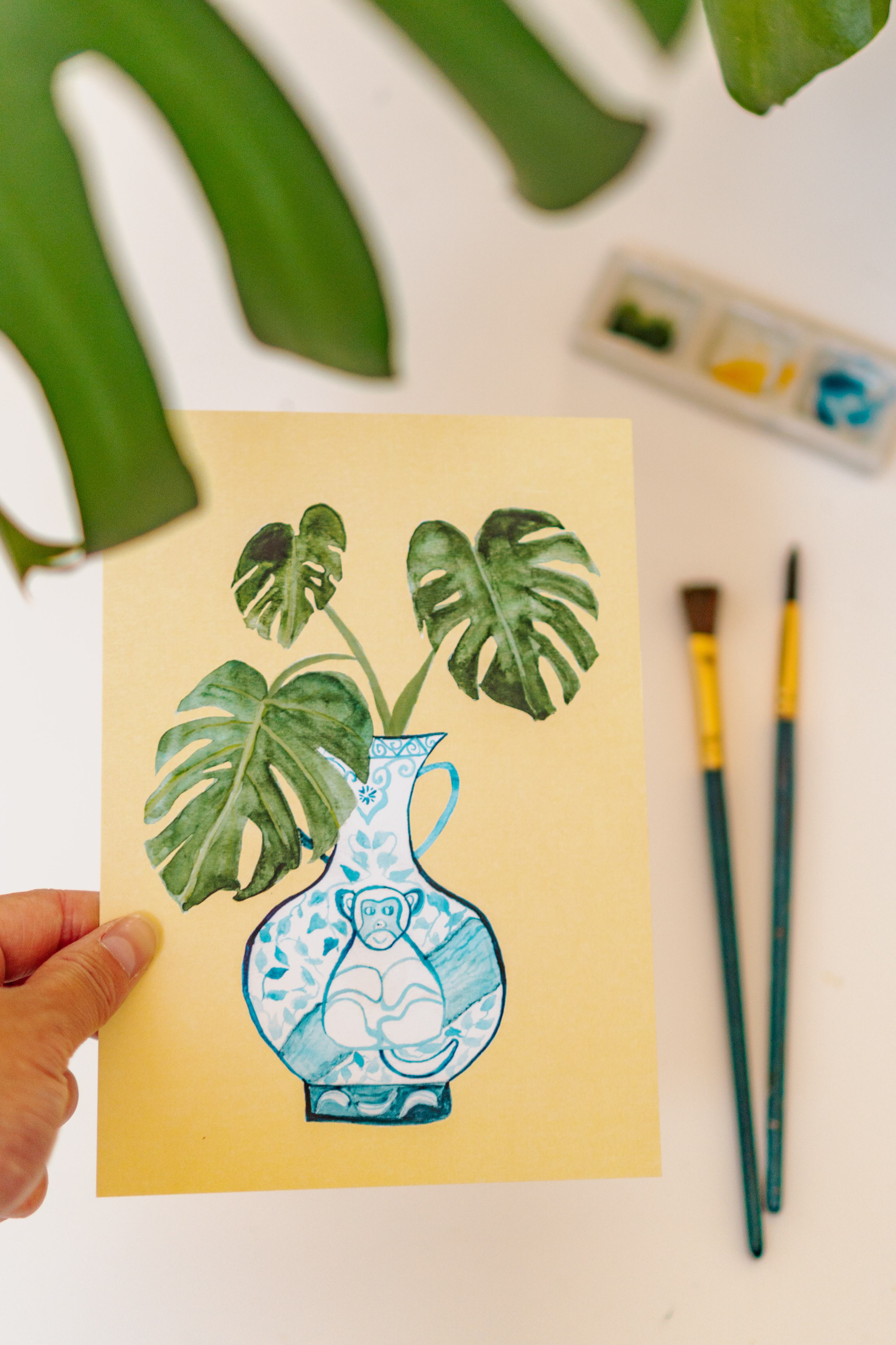 A print of a monstera plant in a blue and white porcelain vase, decorated with a monkey.