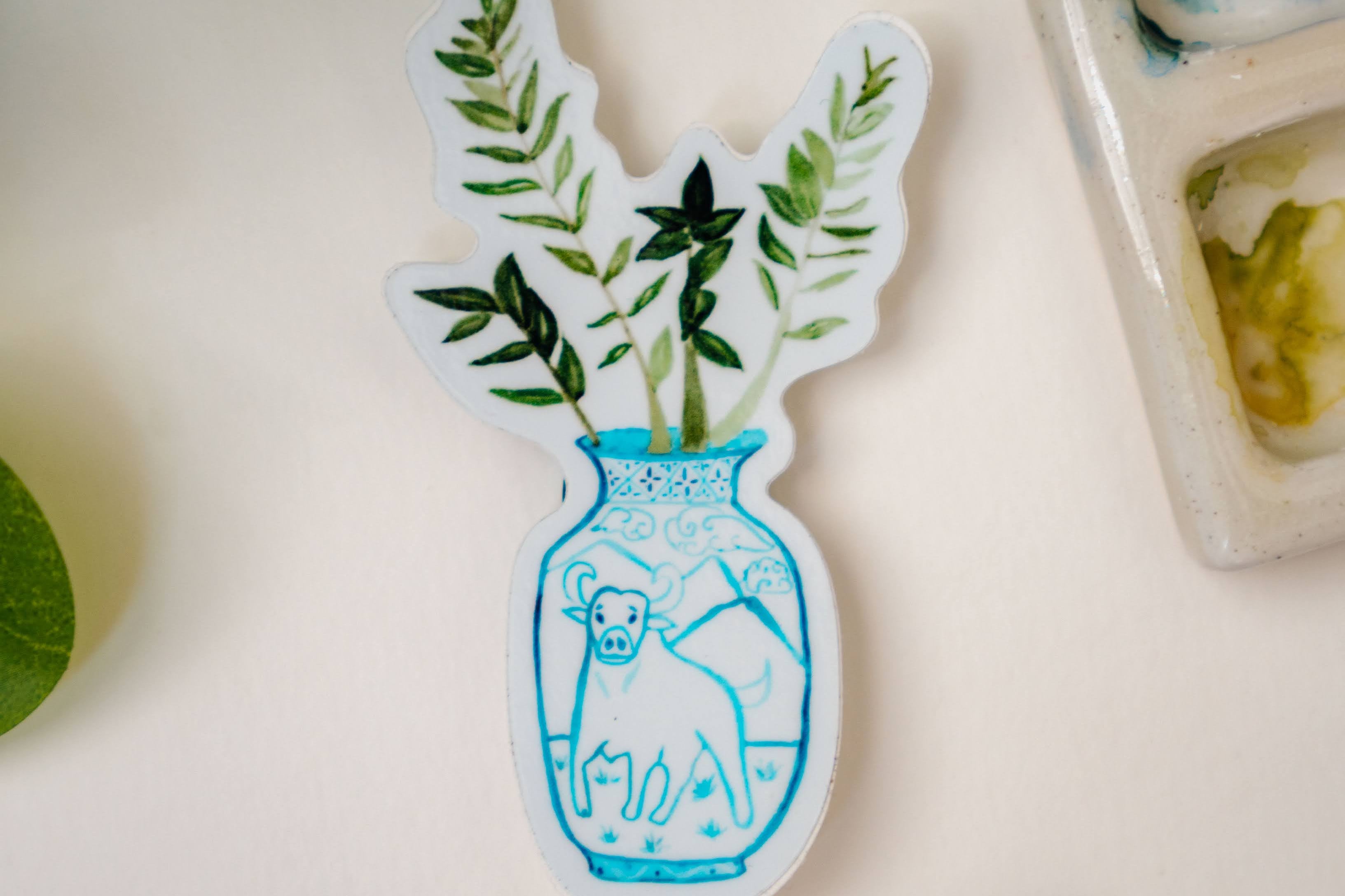 A sticker of a ZZ plant in a blue and white porcelain vase, decorated with an ox.