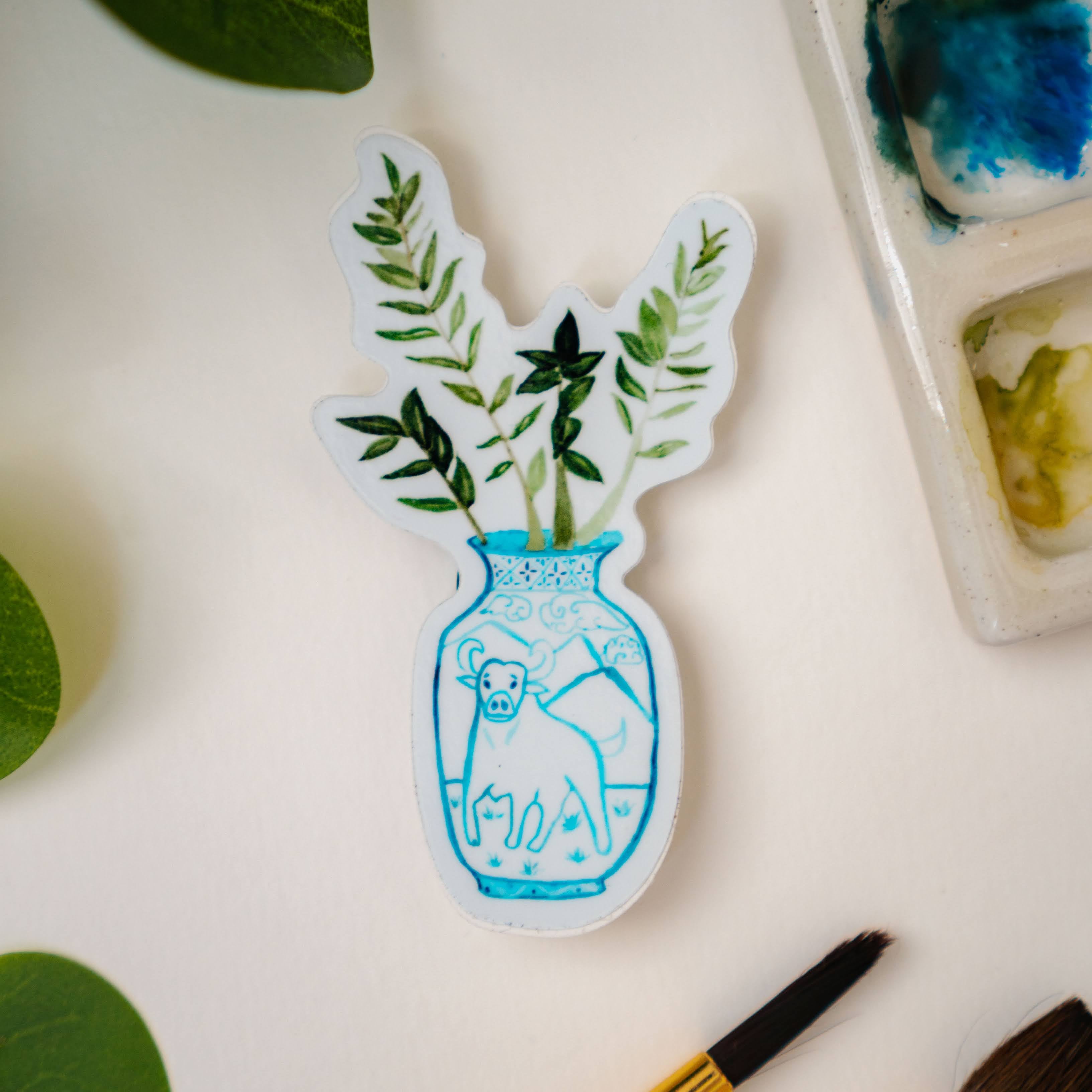 A sticker of a ZZ plant in a blue and white porcelain vase, decorated with an ox.