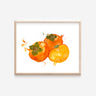 A print of three rich, orange watercolor persimmons. One persimmon is cut open to display the soft yellow-orange inside.