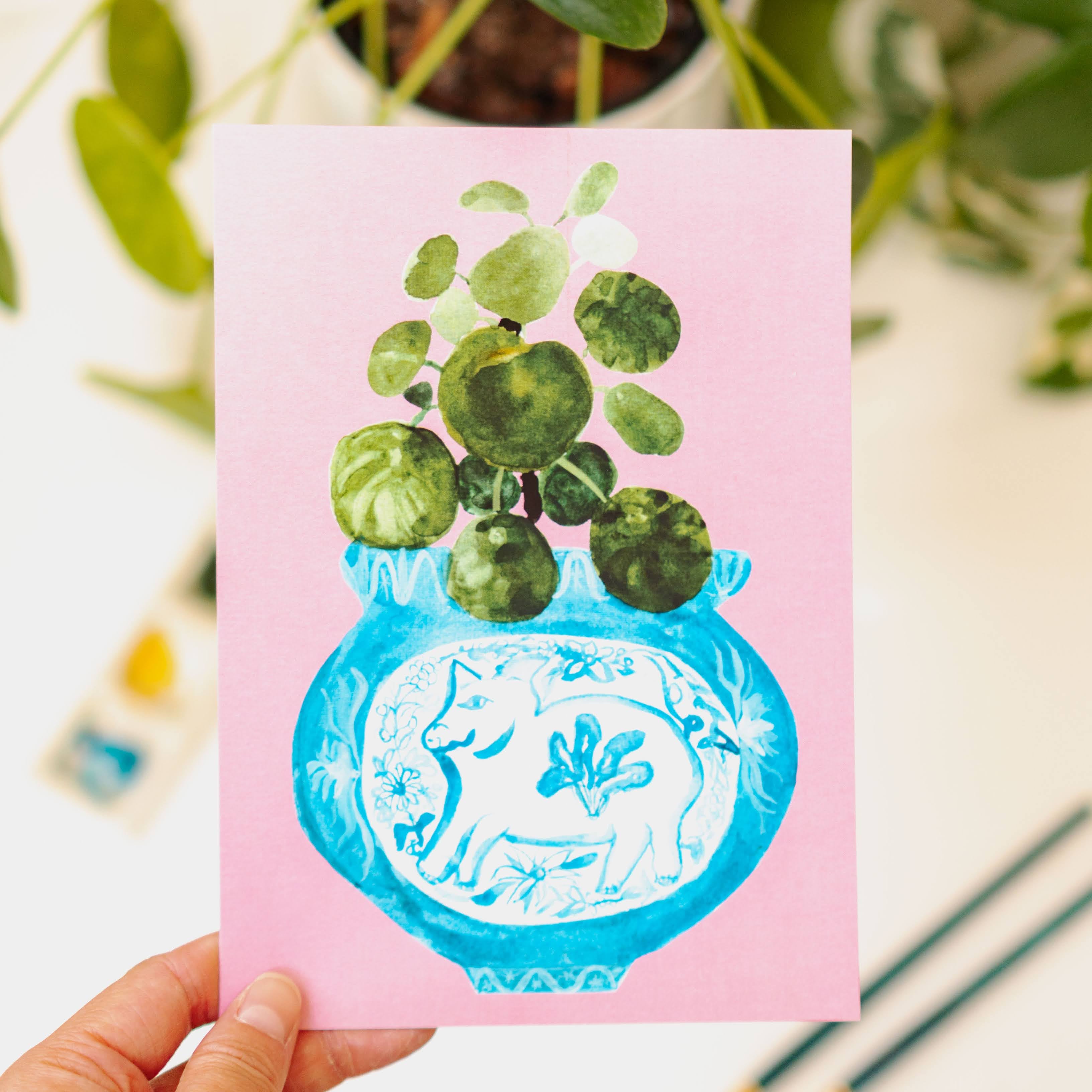 A print of a pilea plant in a blue and white porcelain vase, decorated with a pig.