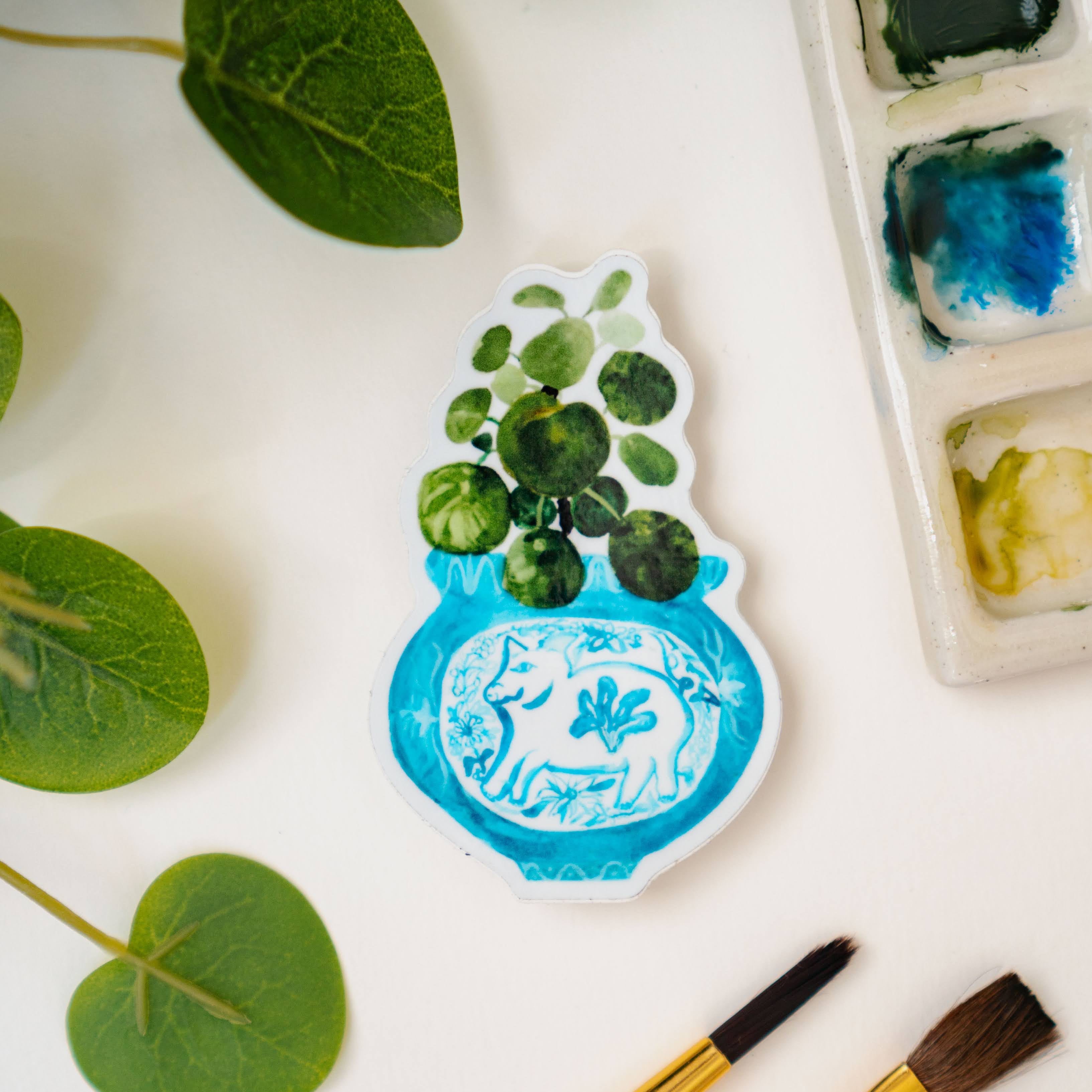 A sticker of a pilea plant in a blue and white porcelain vase, decorated with a pig.