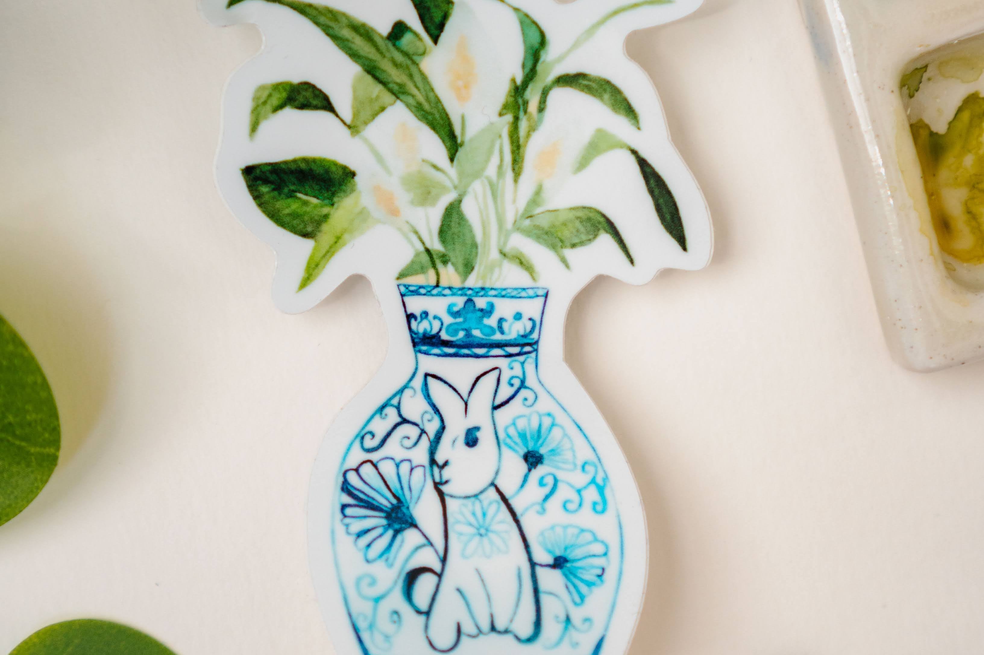 A sticker of a peace lily plant in a blue and white porcelain vase, decorated with a rabbit.