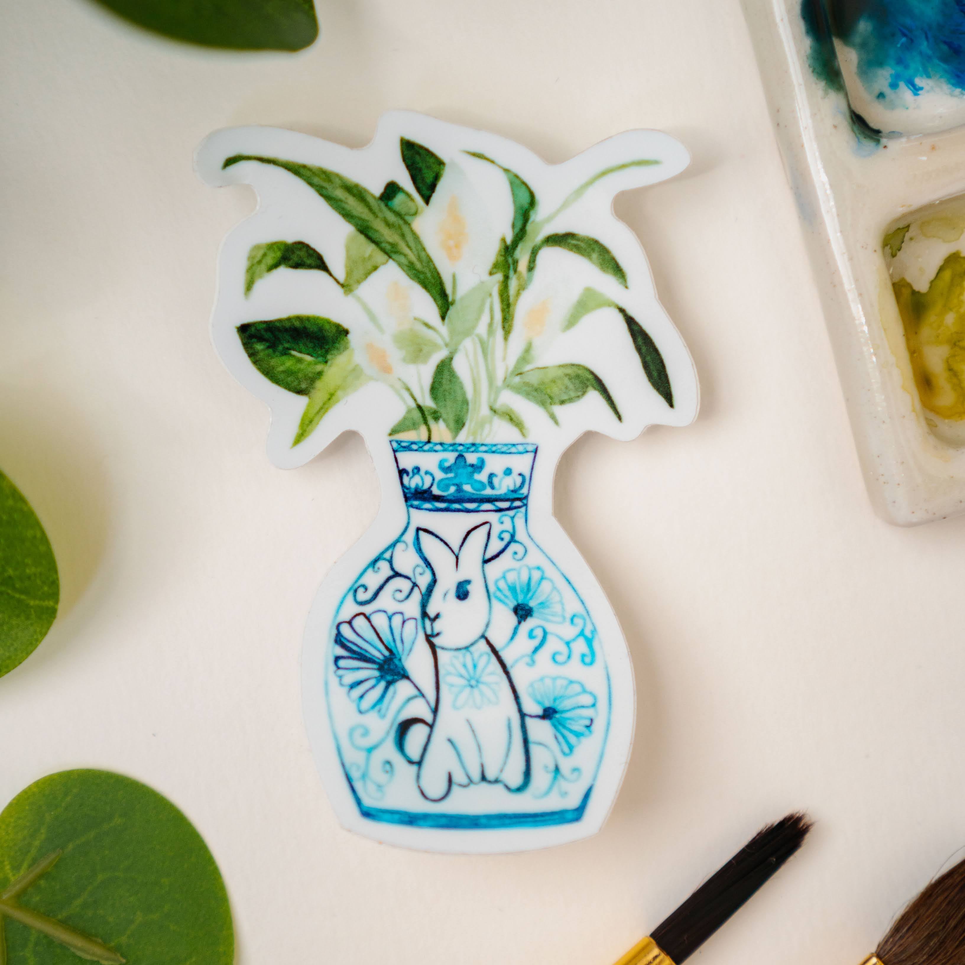 A sticker of a peace lily plant in a blue and white porcelain vase, decorated with a rabbit.
