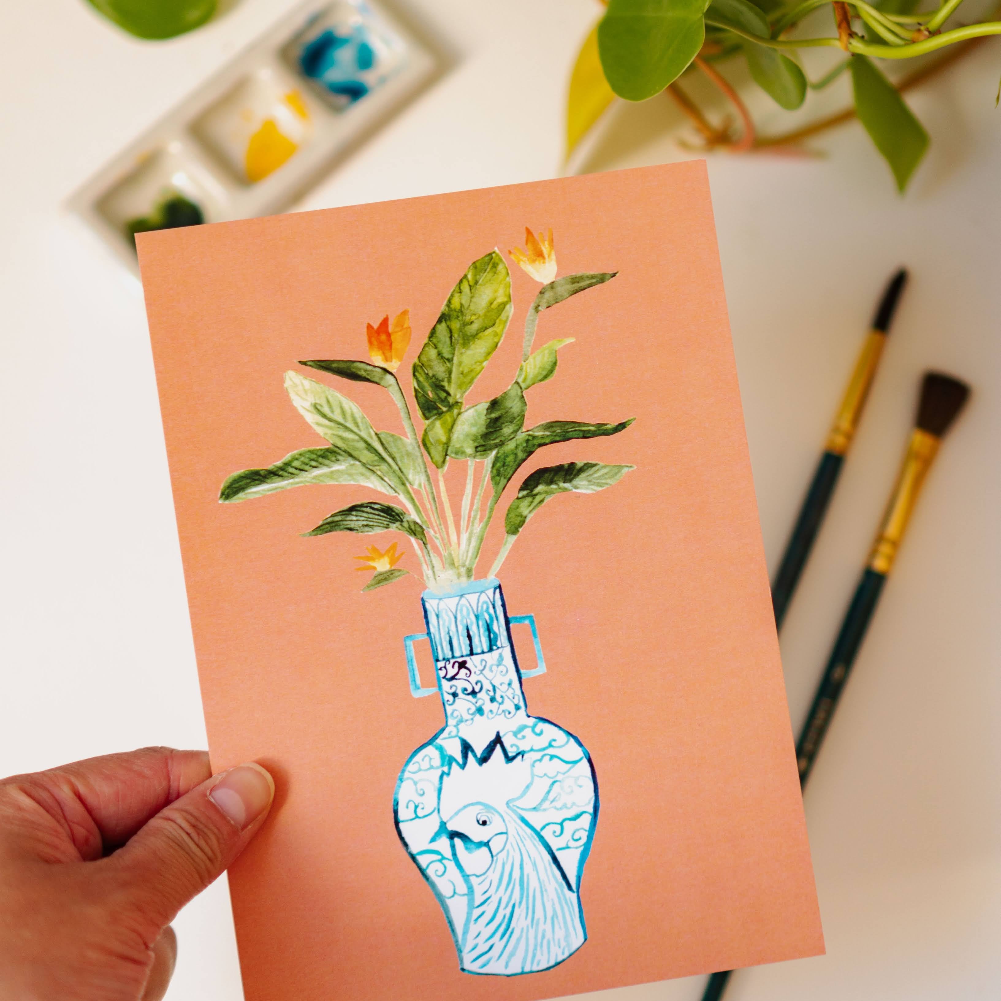 A print of a bird of paradise plant in a blue and white porcelain vase, decorated with a rooster.