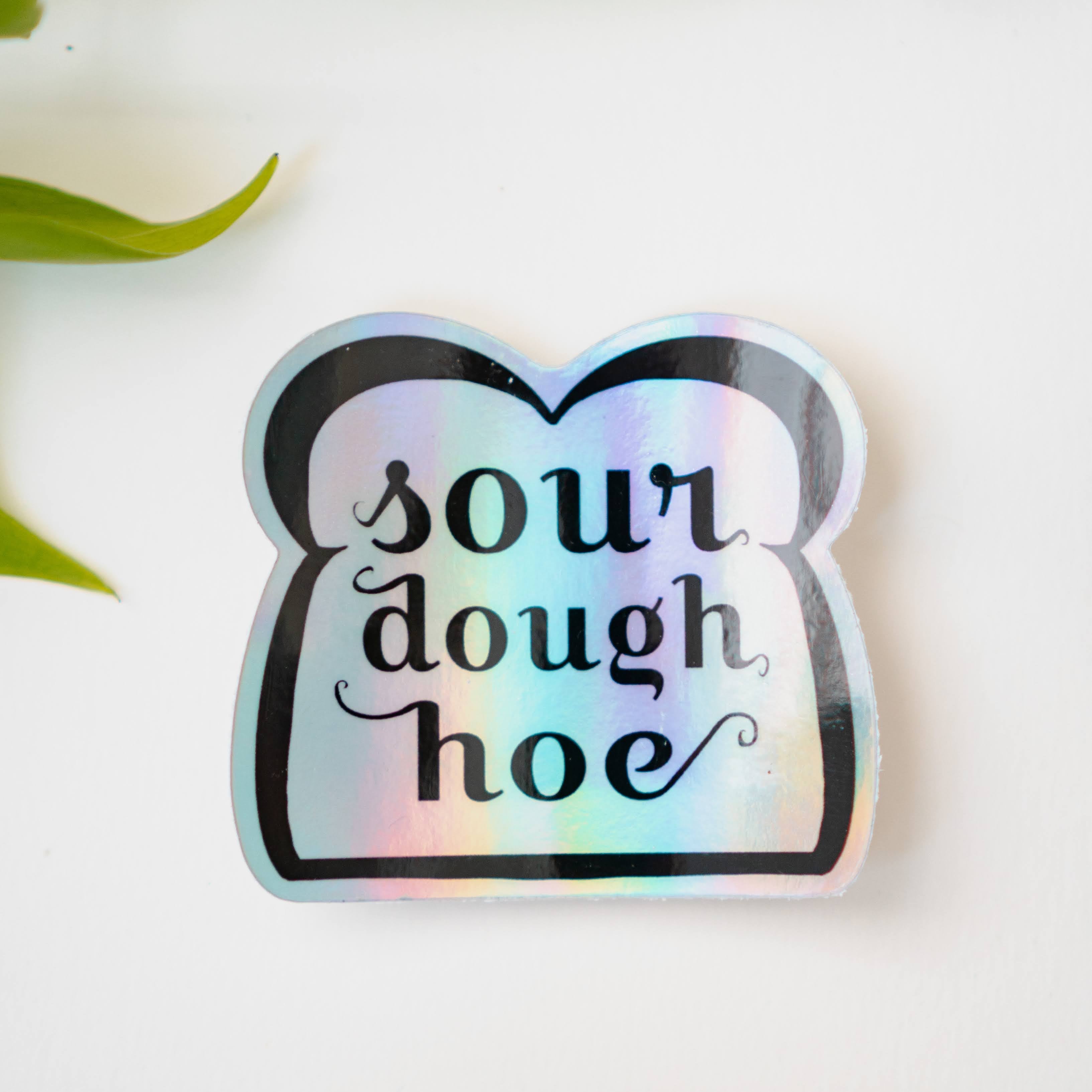 A holographic sticker featuring line art of a slice of bread and the words "sourdough hoe" written in the center.