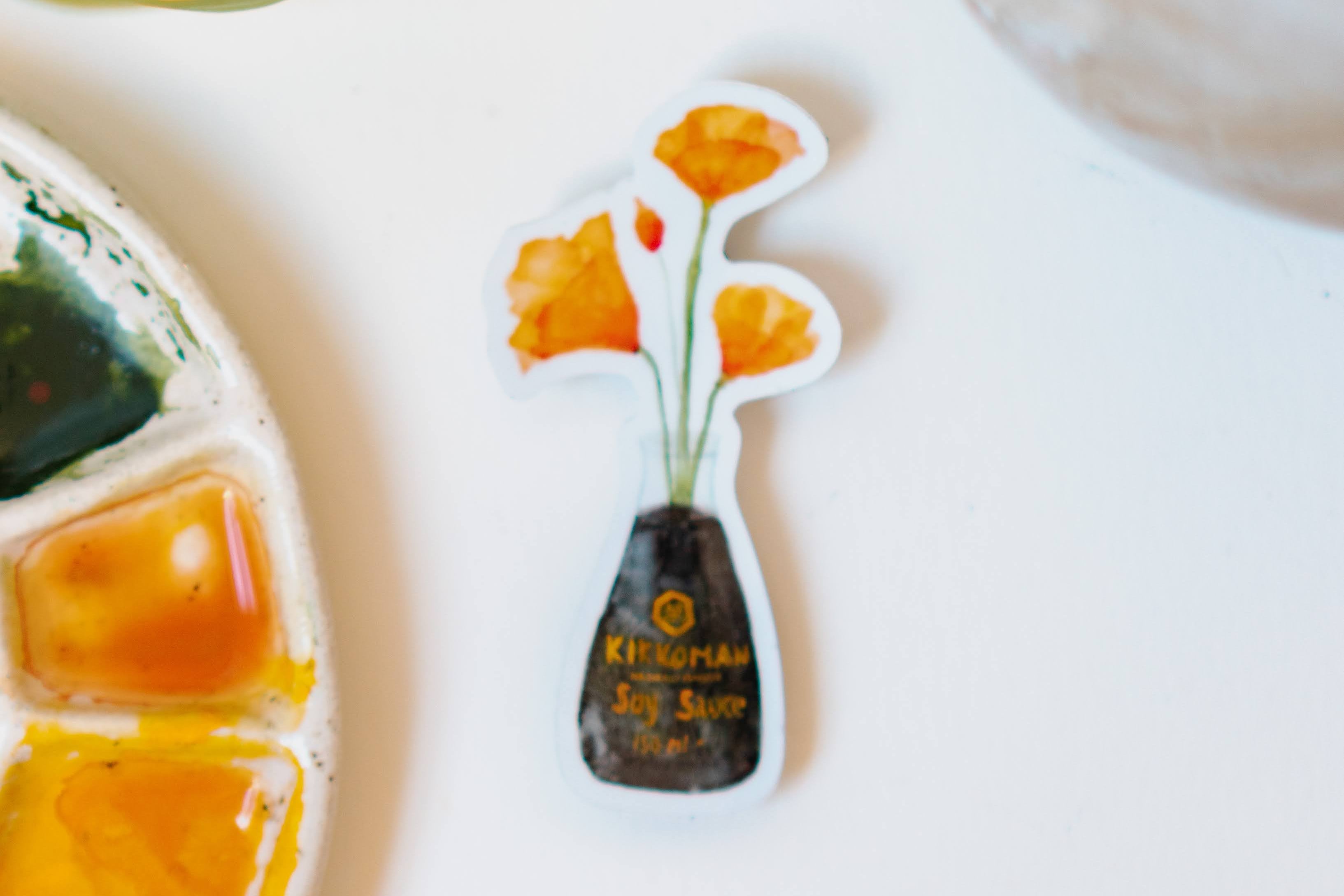 A white sticker of four orange California Poppies in a soy sauce bottle.
